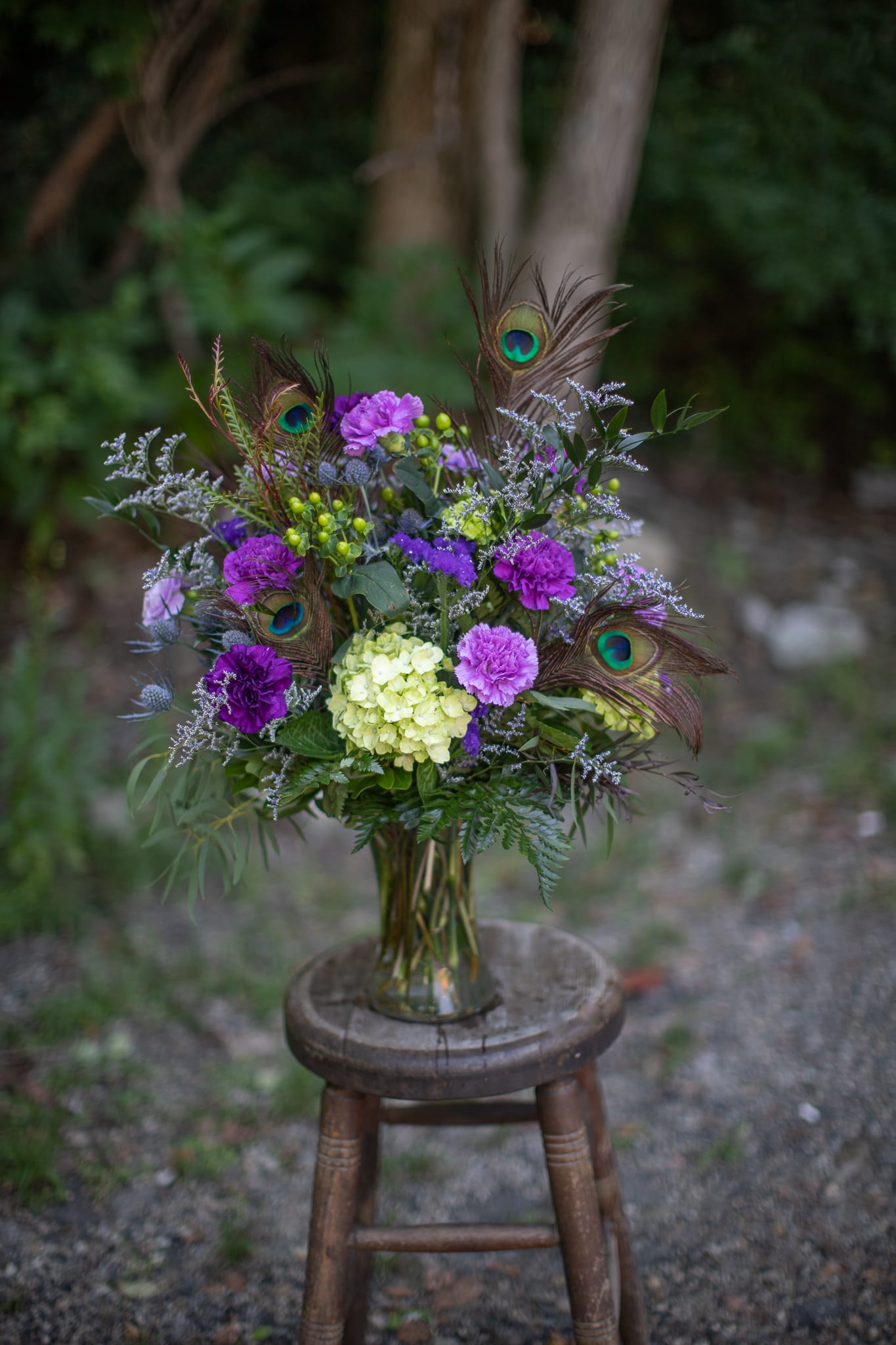 Prince Peacock - Purple is the color of royalty.  Captivate the eye with specialty moon series dianthus ranging in shades from lavender to plum are paired with lime hydrangeas to play on complimentary colors. Contrasting lime berries and blue dynamite thistle give the design texture and more excitement.  Exotic teal colors of shimmering peacock feathers make a bold statement and peak interest in this whimsical floral design. 