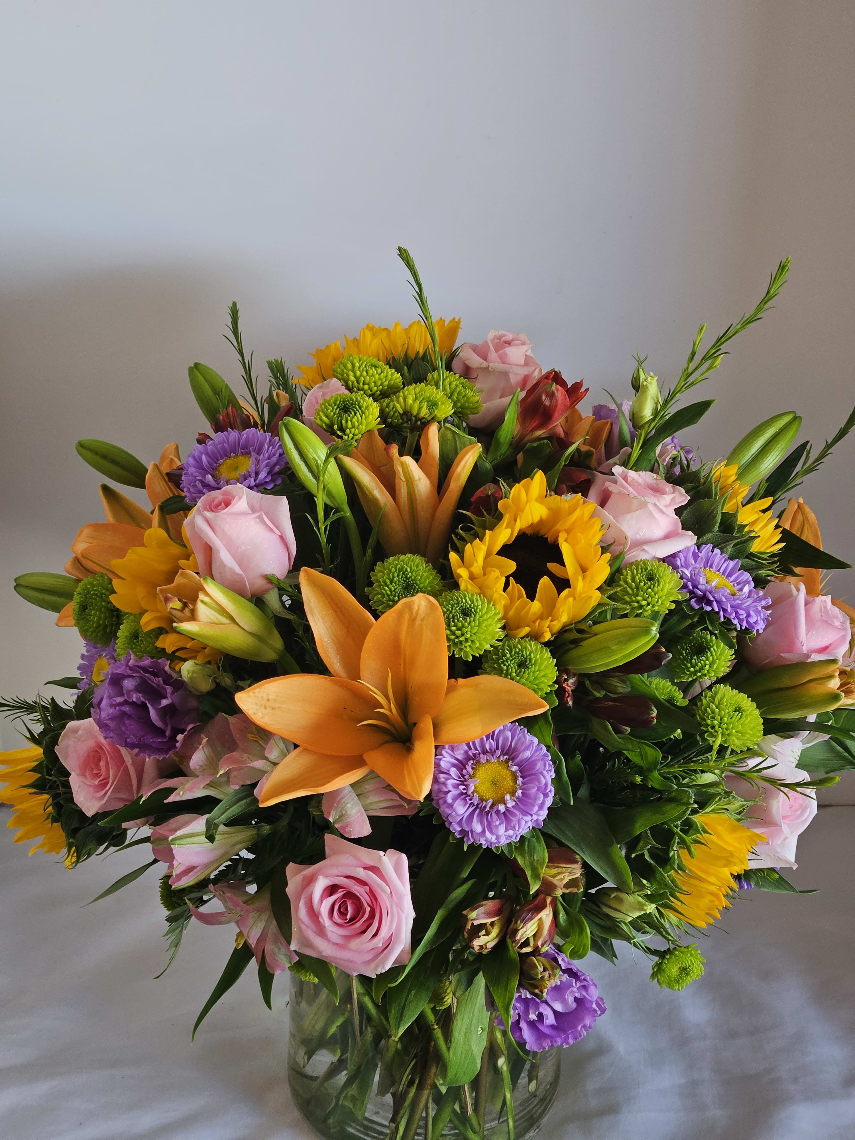 Grand Garden - Luxurious and lasting arrangement consisting of a grand gathering of roses, lilies, sunflowers , stock, alstroemeria and more, beautifully hand-arranged by our professional designers in a posh cylinder vase. FlowerBee's floral artisans hand-design each arrangement, so components may vary due to local availability  Lilies may arrive in bud form and will open to full beauty over the next 2-3 days.