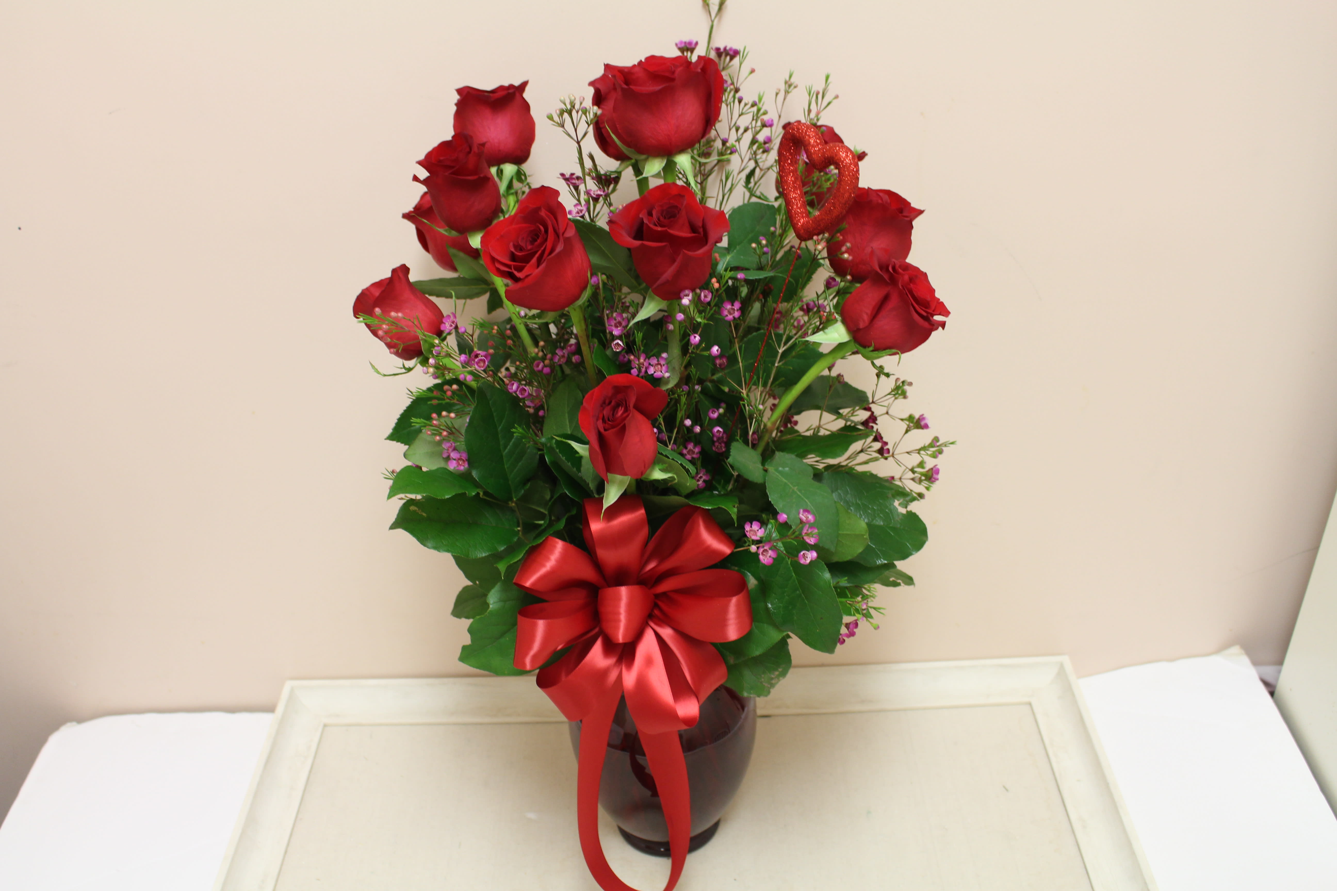Let your love shine.  No babies breath, beautiful wax flower - A dozen red roses arranged in a vase with lemon, myrtle, and beautiful wax flower. All in a red mercury vase.
