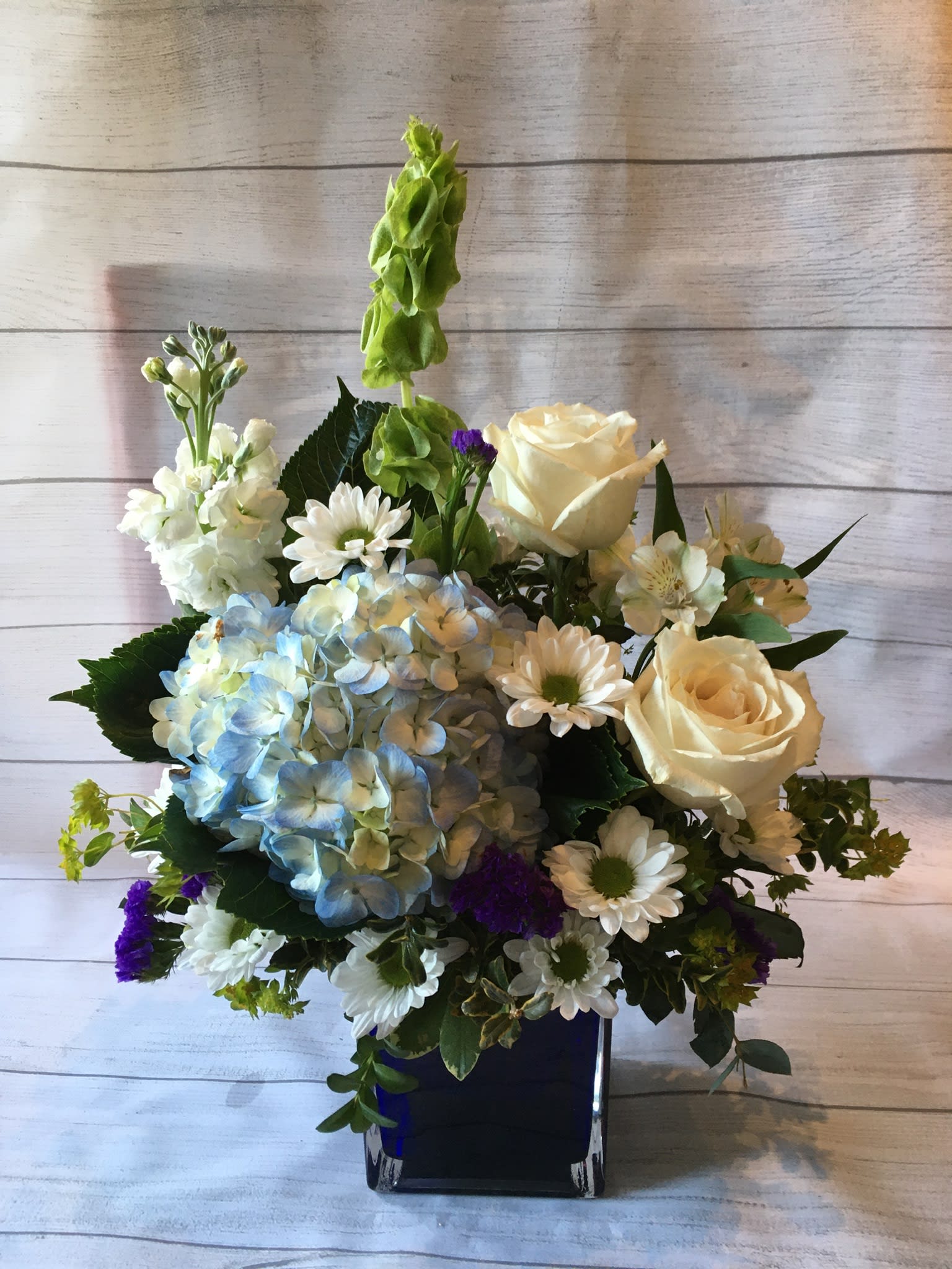 Blue and white design Blue and white design - A refreshing combination of blue and white flowers in a blue cube will put a smile on your special someone’s face.