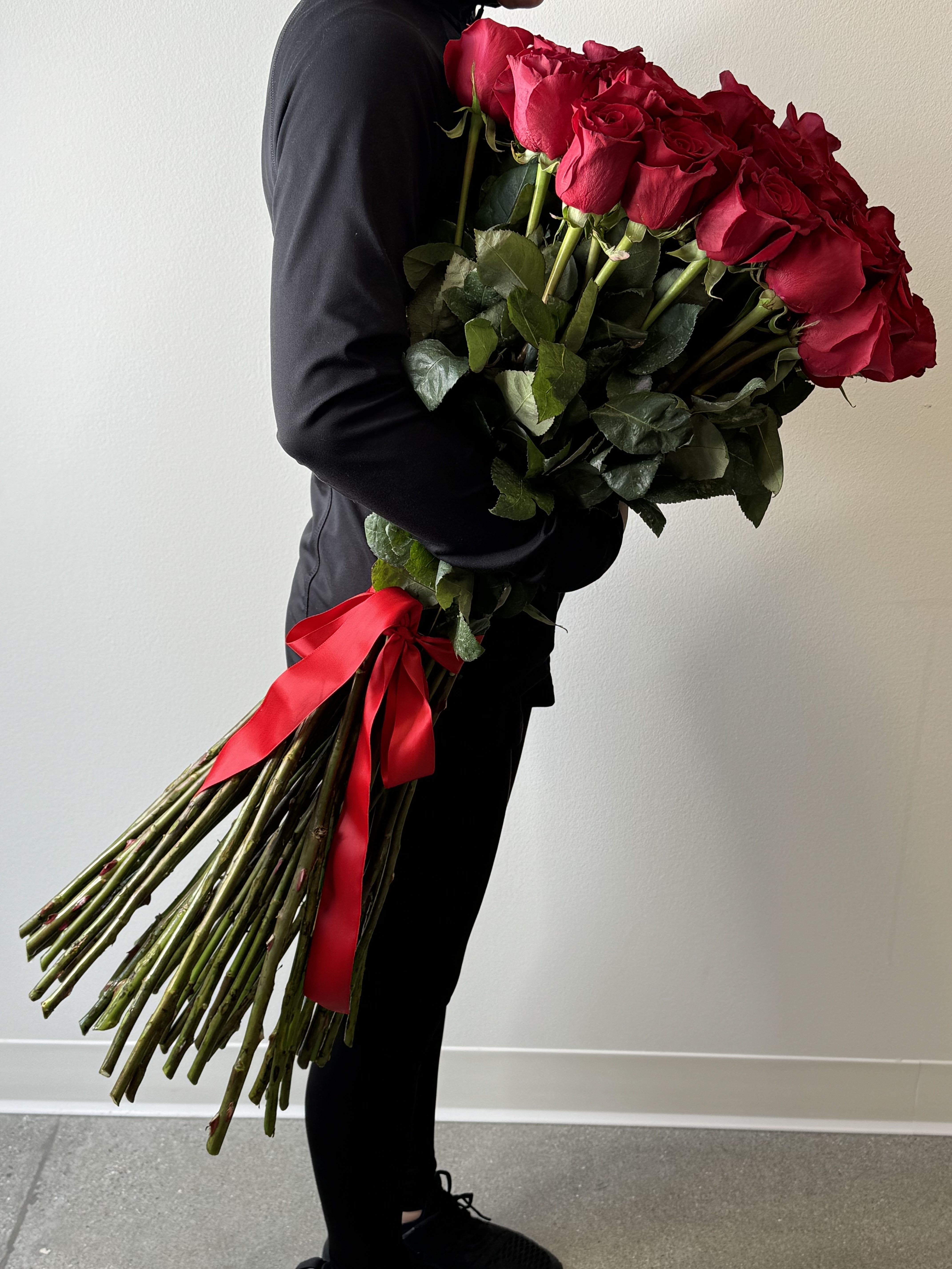 Ultra Long Stemmed Red Roses - Prepare for a love story of epic proportions with Irvine Village Flowers’ breathtaking masterpiece—50 ultra long-stemmed red roses, a towering declaration of devotion! Ordered with a whisper of anticipation at least one week in advance, these majestic blooms stretch nearly 3 feet tall, bundled and tied with a silken red ribbon that flutters like a lover’s promise. Delivered in a tall, clear cylinder vase, this arrangement is a grand gesture, a cascade of passion that fills the air with romance and awe.  Each rose tells a timeless tale: these crimson beauties, bold and velvety, sing of love so deep it echoes through the ages, their ultra-long stems reaching for the heavens in adoration. The red ribbon weaves them together, a scarlet thread of unity and ardor, while the vase stands as a crystal throne, showcasing their splendor. From Irvine Village Flowers, this is more than a bouquet—it’s a monument to the heart. Plan ahead, visit us in-store or online, and let our meticulous delivery bring this towering romance to your beloved, fresh and ready to sweep them off their feet in a sea of red.