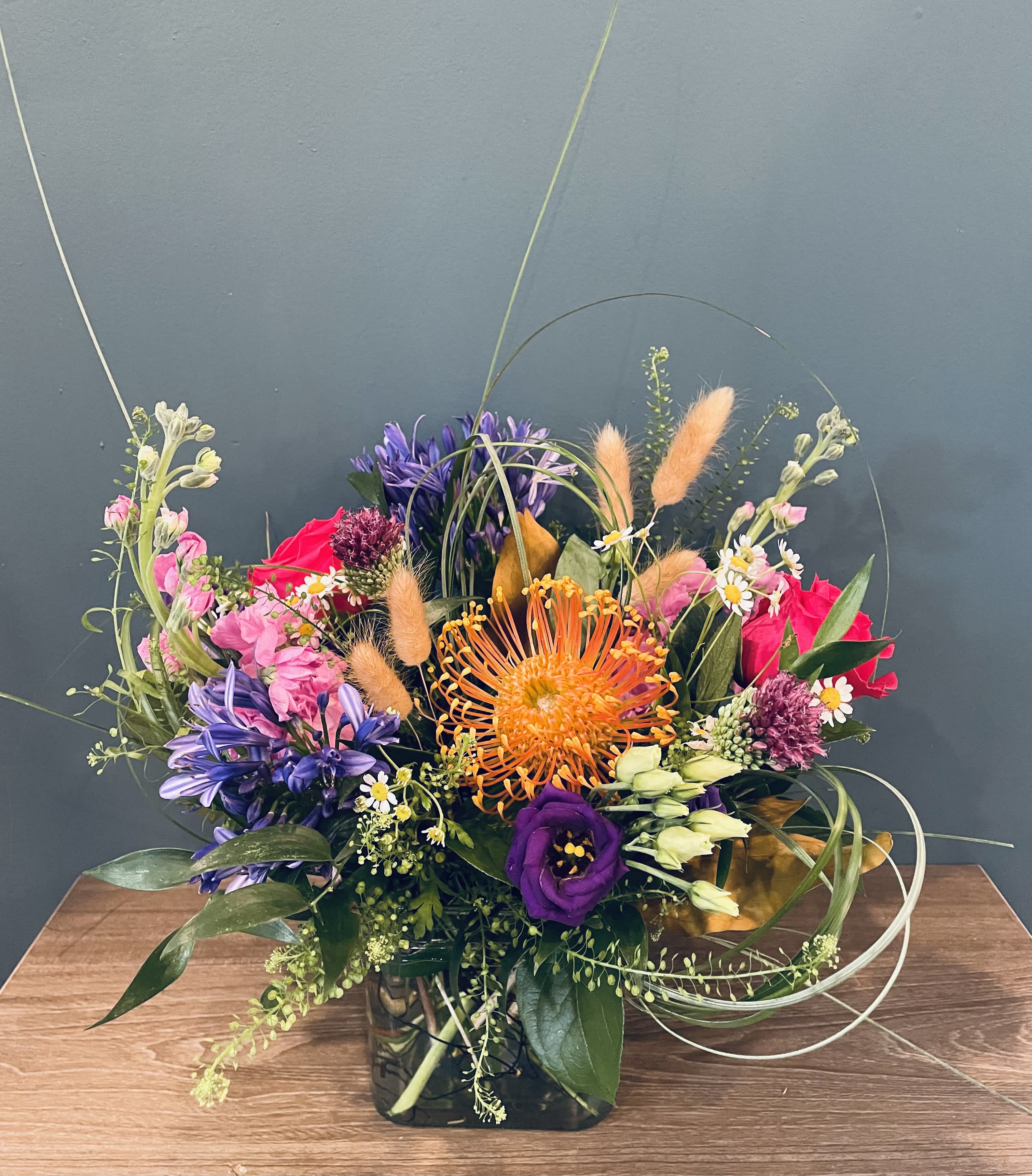 Wild and Free - A bright mix of fun flowers, including pin cushion protea, agapanthus, allium, lisianthus, roses, stock, bunny tails and a mix of greenery. 