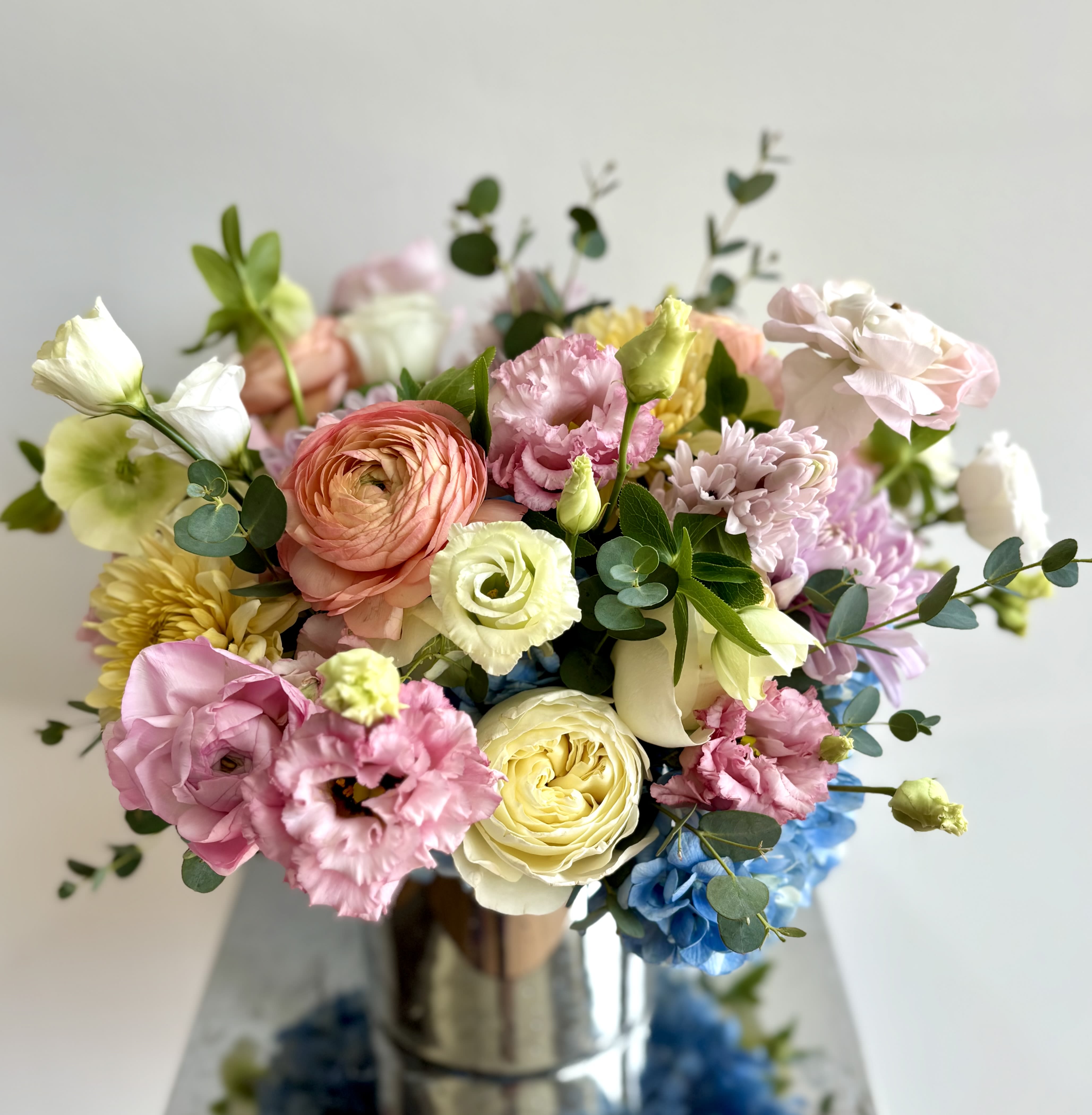 Smitten With Love - A lovely flower arrangement for those who love flowers in pastel color tones. The flower mix usually consists of light blue hydrangeas, roses, ranunculus, mini orchids and dahlias when available, and additional premium fillers and foliage to make the arrangement look lush. I always work with premium flowers, all arranged in a beautiful vase to complement the flowers. 