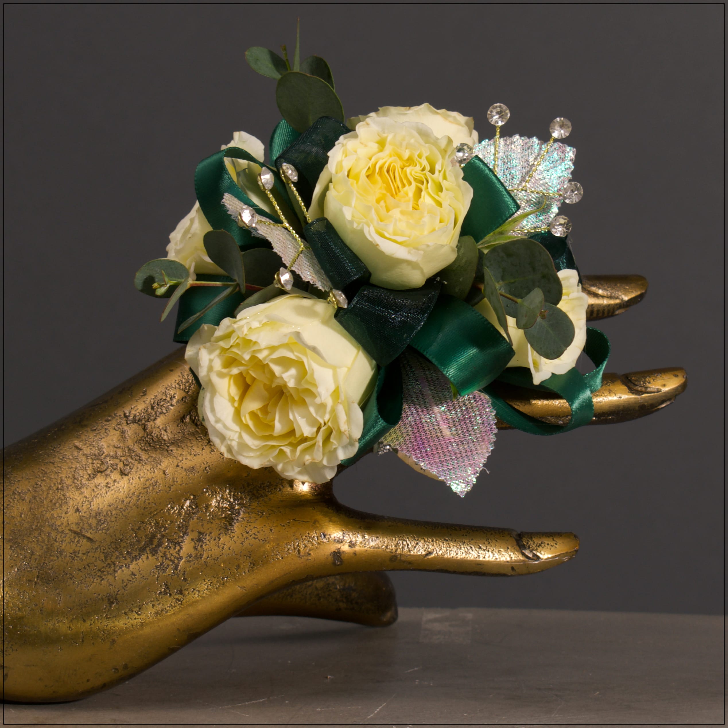 Lauren- Wrist Corsage Lauren- Wrist Corsage - Buttercream Roses with Rhinestone Sprays and Iridescent Leaves on a Silver Glitter band with Emerald Green Ribbon.