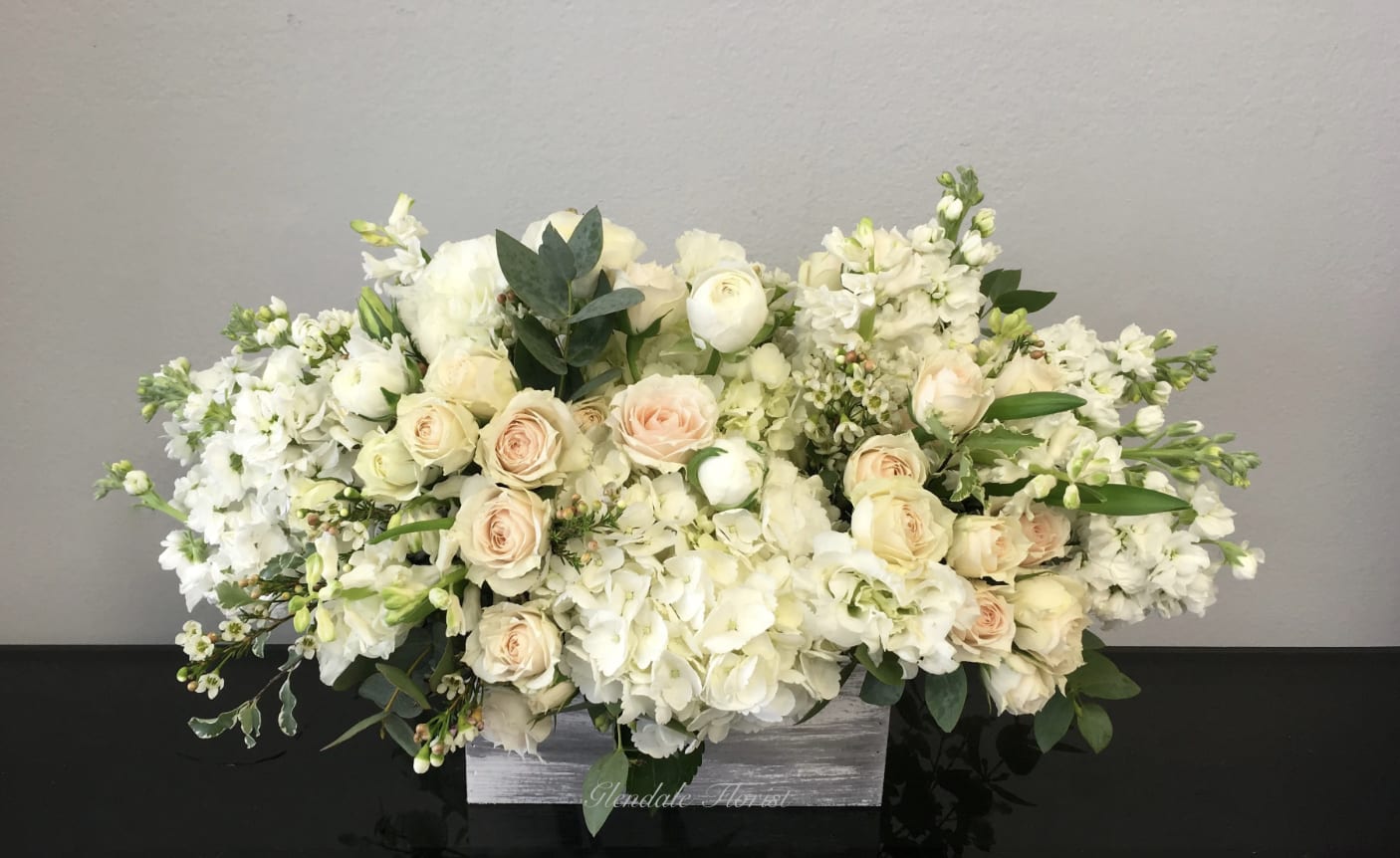 White Dream - LA - All white hydrangeas, roses, stock, and seasonals carefully arranged in a birchwood box. It stands approximately 14-16'' tall and approximately 26'' wide. 