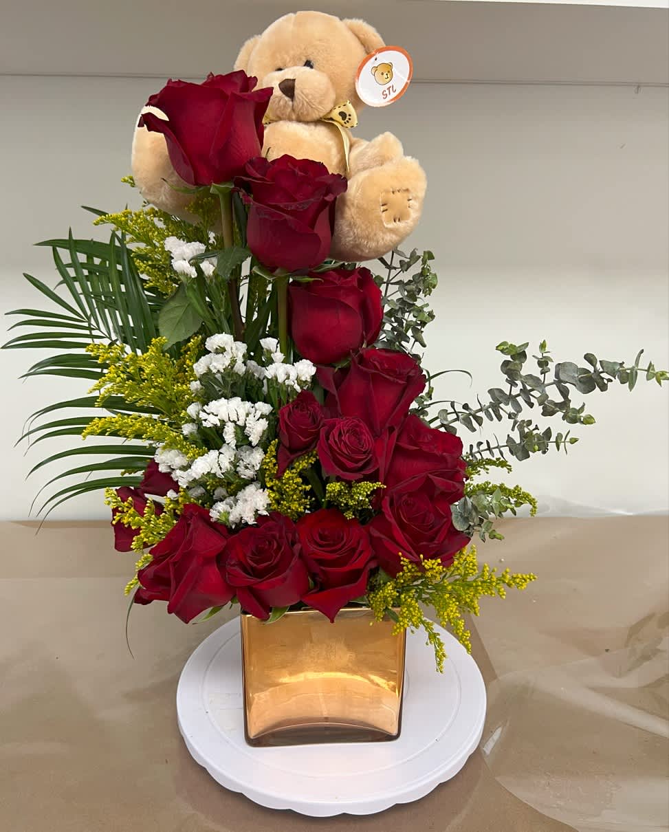 Roses and Teddy Bear Arrangement Roses and Teddy Bear Arrangement - Dozen roses (color may change upon request and availability) in a square glass vase, decorated with a teddy bear, white limonium, eucalyptus, solidago (golden rods), and palm leaves.