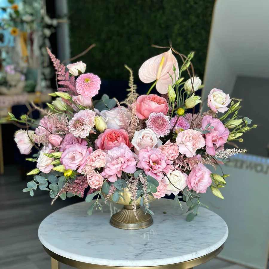 Pink Heaven - The Modern Elegance Arrangement in a gold vase is a stunning display of sophistication and charm. Featuring vibrant pink lisianthus, delicate anthurium, feathery astilbe, and classic pink roses, this arrangement creates a harmonious and romantic color palette. Branches add height and drama, while fragrant eucalyptus provides a fresh scent and soft greenery. Designed to blend contemporary style with timeless floral beauty, this arrangement is perfect as a centerpiece for baby showers, birthdays, or any special occasion. 
