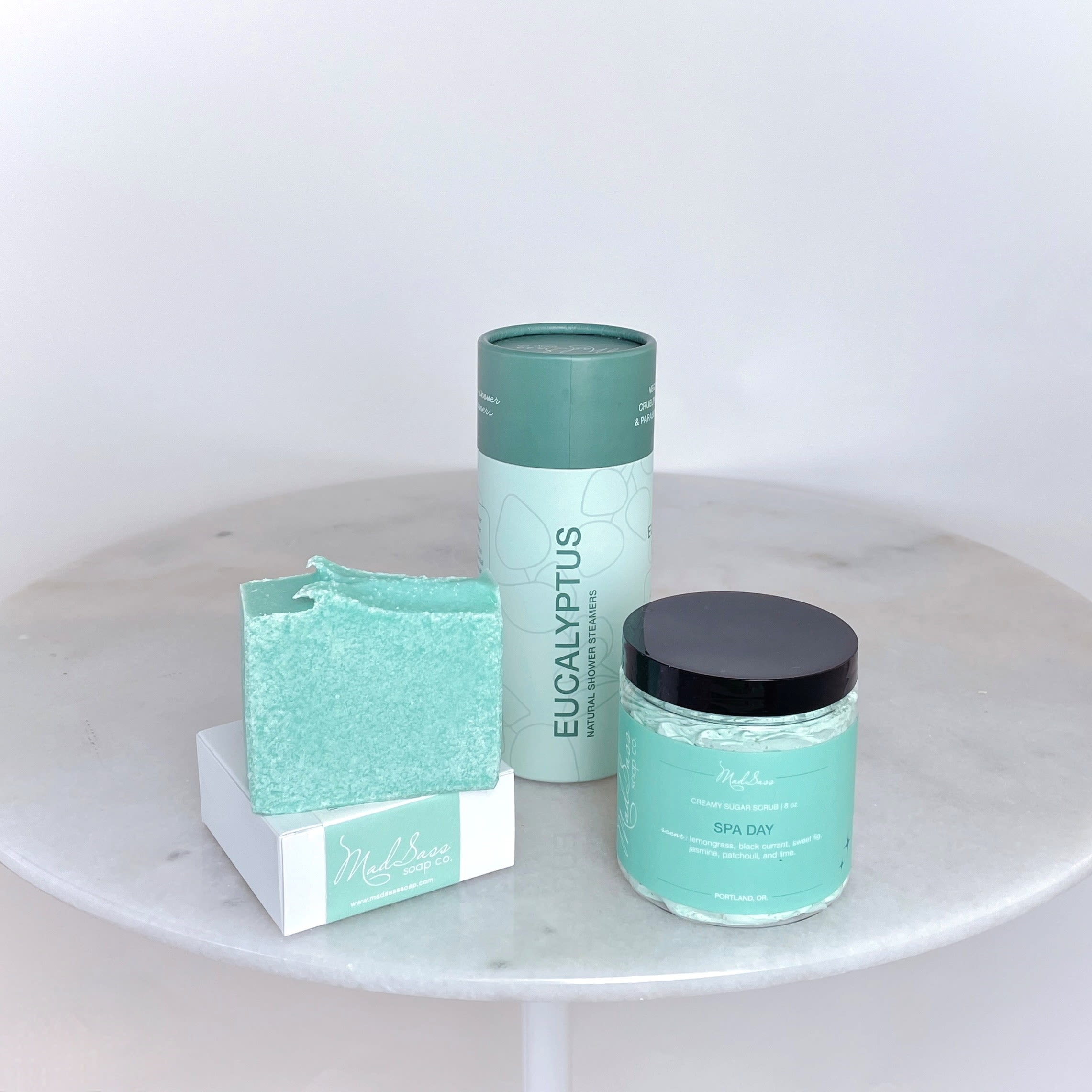 Spa Day Collection - Standard - We have partnered with a local Portland favorite, Mad Sass, to bring you the Spa Day collection that you can order on its own (and delivered within our delivery range) or add to your flower arrangement / plant to make your gift extra special.  Spa Day is a clean-smelling, beautiful, and luxurious scent with notes of lemongrass, black currant, sweet fig, jasmine, patchouli, and lime. Create your own spa at home whenever you use these products!  The Standard size includes Spa Day Soap and Creamy Sugar Scrub along with the Eucalyptus Natural Shower Steamers (pack of 5 pucks). Upgrade to the Deluxe size to add a matching Soy Wax Candle (burn time 60+ hours!) and the most adorable sage-green tipped fancy matches (~75 in each bottle) from local vendor, Frankie &amp; Claude.