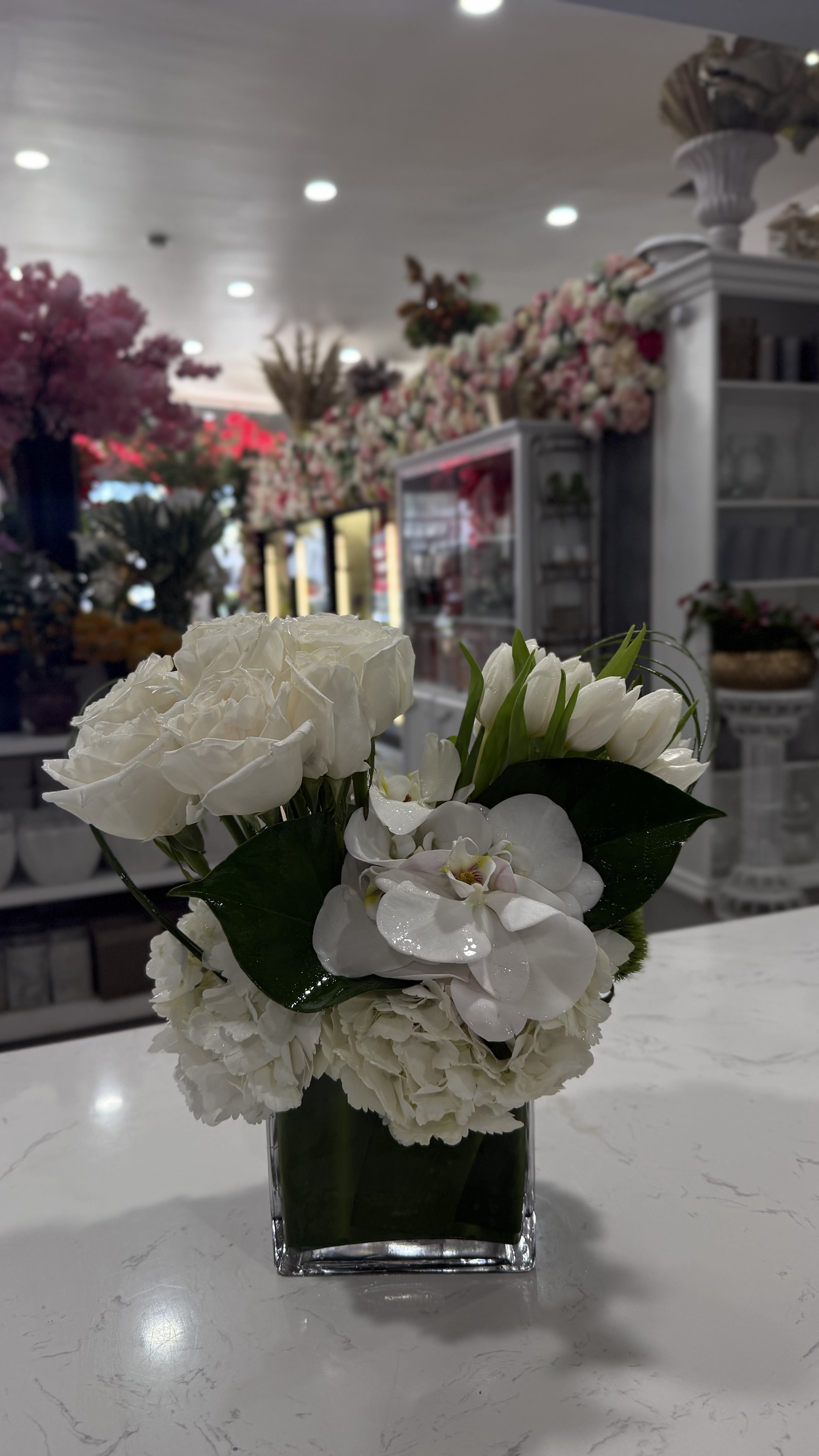 Cloud Nine - Crisp white roses, tulips, hydrangeas, and phalaenopsis orchid come together in a chic, compact design wrapped in glossy greens. Cloud Nine is a clean, modern statement—perfect for stylish interiors, luxe events, or sending a message of pure elegance.