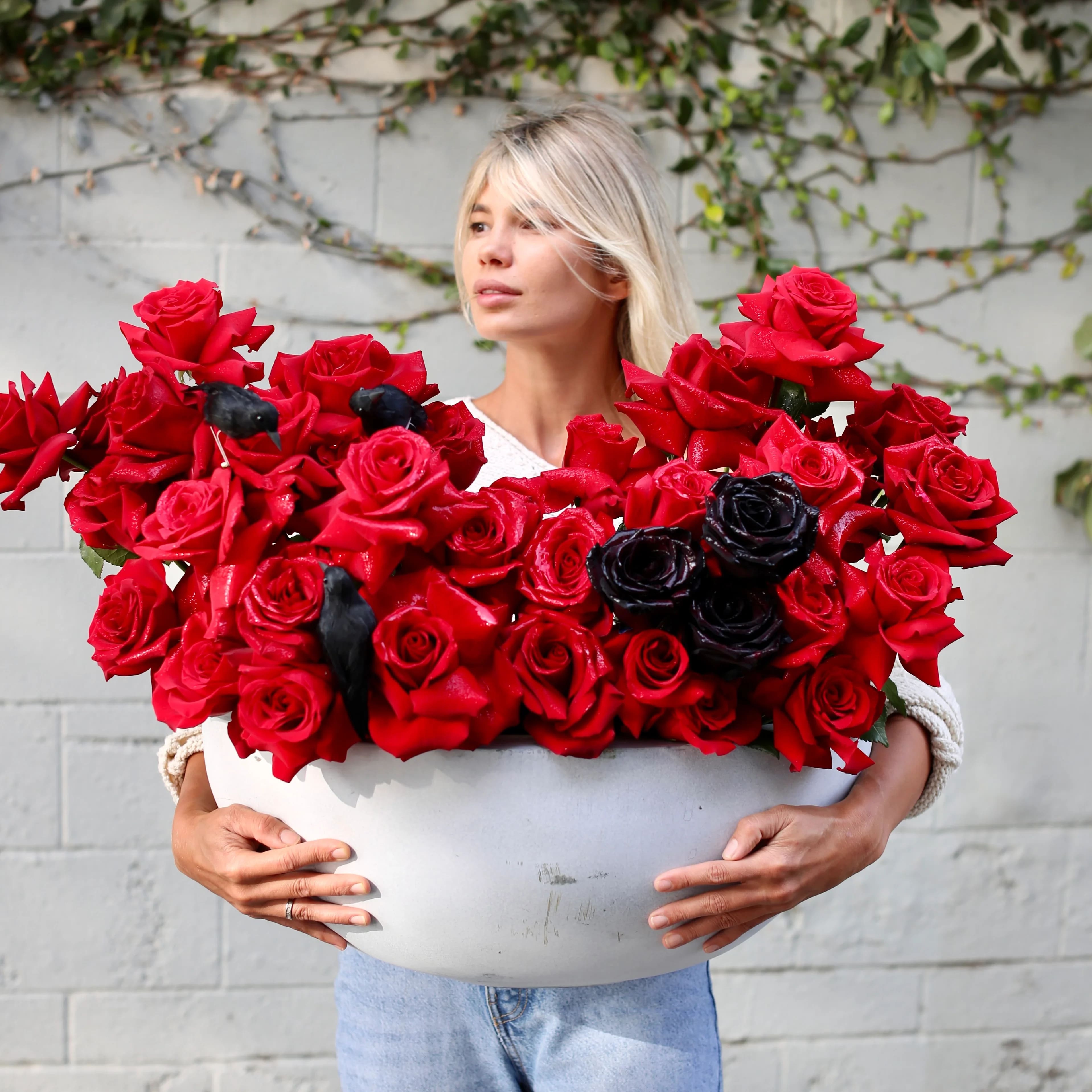 Amore - Amore is a luxury flower arrangement featuring rich red and black roses, accented with dramatic ravens, making it a one-of-a-kind design. Assembled in a premium stone vessel, this arrangement is perfect for romantic occasions, Halloween parties, or any event needing an outstanding floral accent. Its unique design adds a touch of mystery and elegance to any setting. 