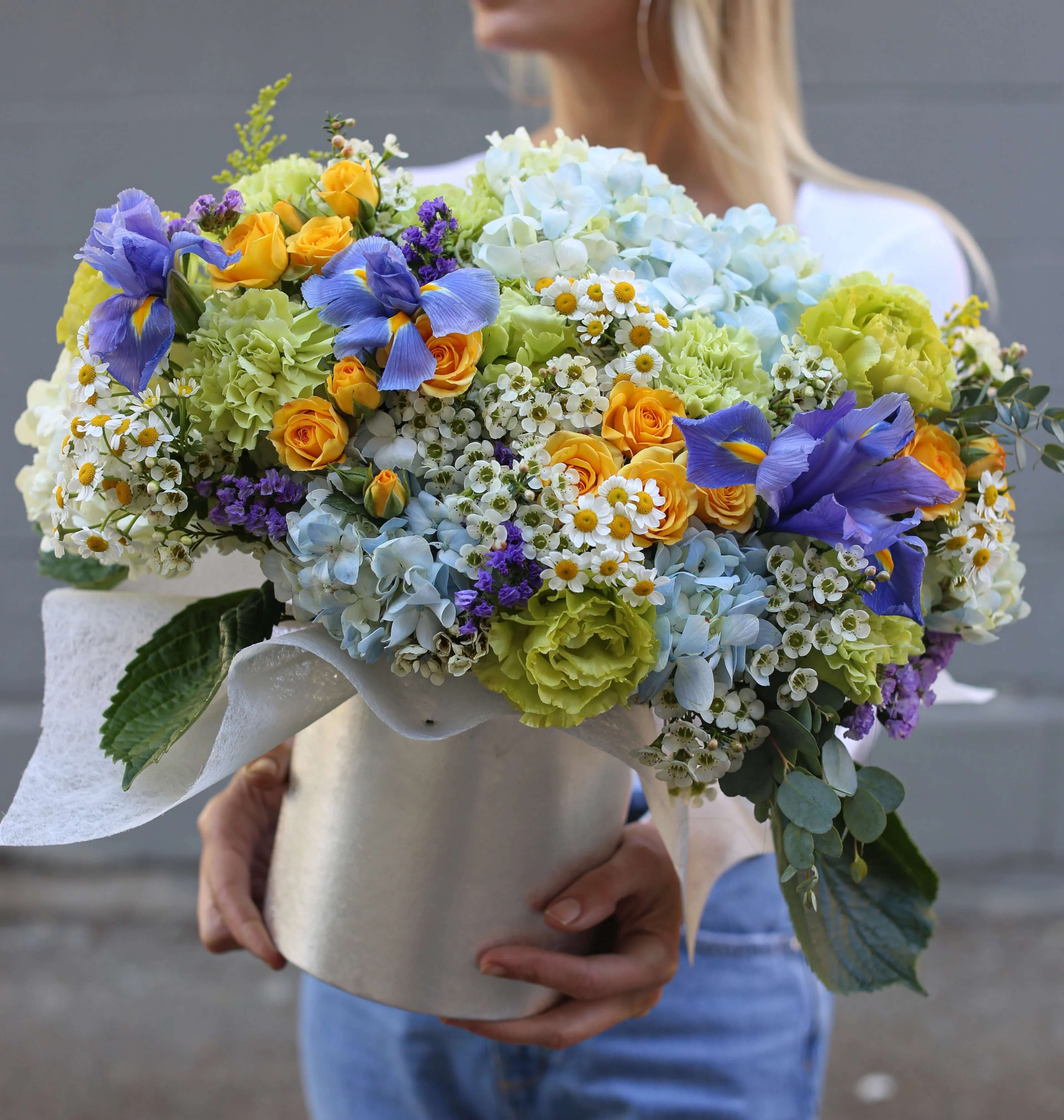 Sofia - Spring box with irises is a colorful floral arrangement with yellow roses, white or blue hydrangea, green carnations, daisies, and irises designed in a box.