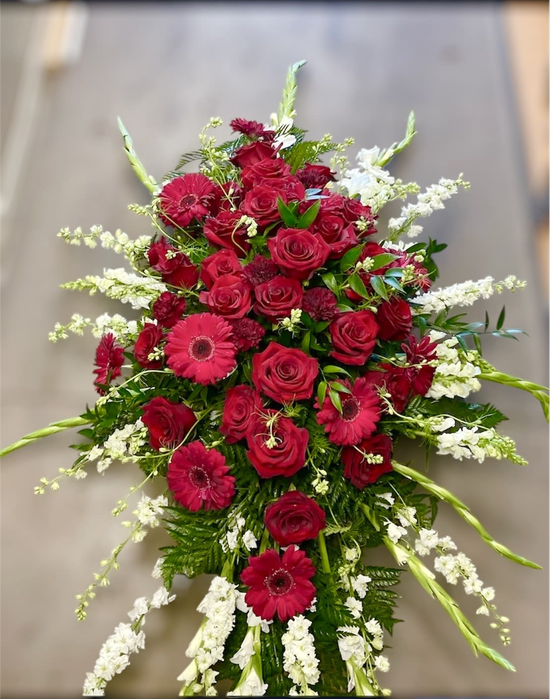 Casket Spray Casket Spray - Theme Colors: Shades of red, white and green Featured Blooms: Roses, Carnations, Gladioulus and greens HK Flowers have a uniqueness of florals and seasonal blooms, certain flowers or colors may not be available as each season affects the availability, color, size, and shape of each floral bloom. Some flowers may be substituted accordingly. Photos are used as a reference for the color palette and is NOT indicated of the final product. We ask for your trust in us that we will pick out the best seasonal available blooms, while still capturing the arrangements theme and colors mentioned above.