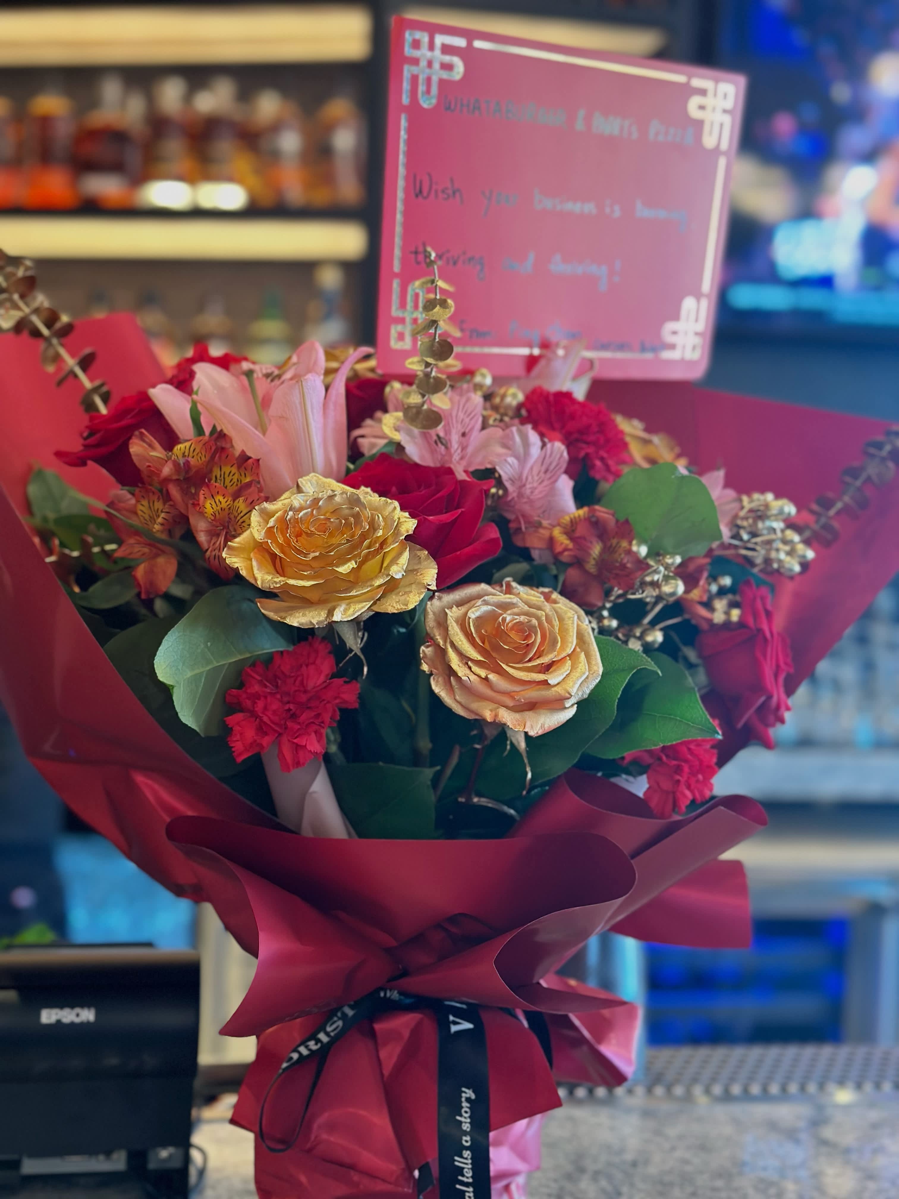 Red grand opening flower vase arrangement - The future has never shone brighter than now. Send your best wishes to a new business grand opening with this flower arrangement. The arrangement features roses in gold and red color, carnations in red color, pink lilies, and red alstroemeria.