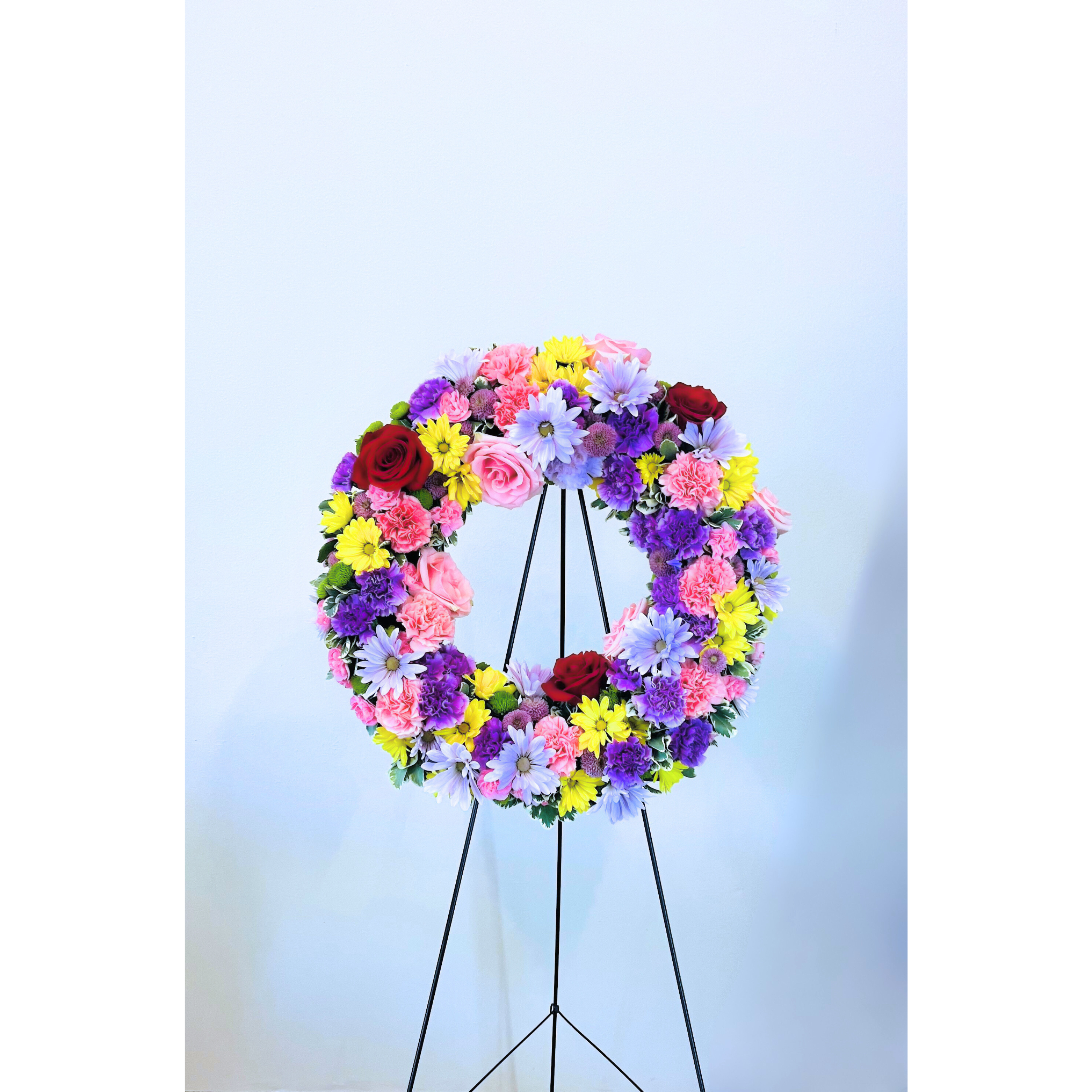 Forever Cherished - &quot;Forever Cherished&quot; can certainly be designed as an easel-standing floral arrangement for a funeral service. With its vibrant colors, including rich reds, bright oranges, deep purples, and soft pinks, it serves as a lively and respectful tribute, celebrating the memory of a loved one. The bold and cheerful mix of roses, lilies, and carnations is intended to bring a sense of warmth and joy while honoring the life and spirit of the departed. This easel-standing arrangement creates a dignified yet colorful focal point, offering comfort and remembrance to all who gather.