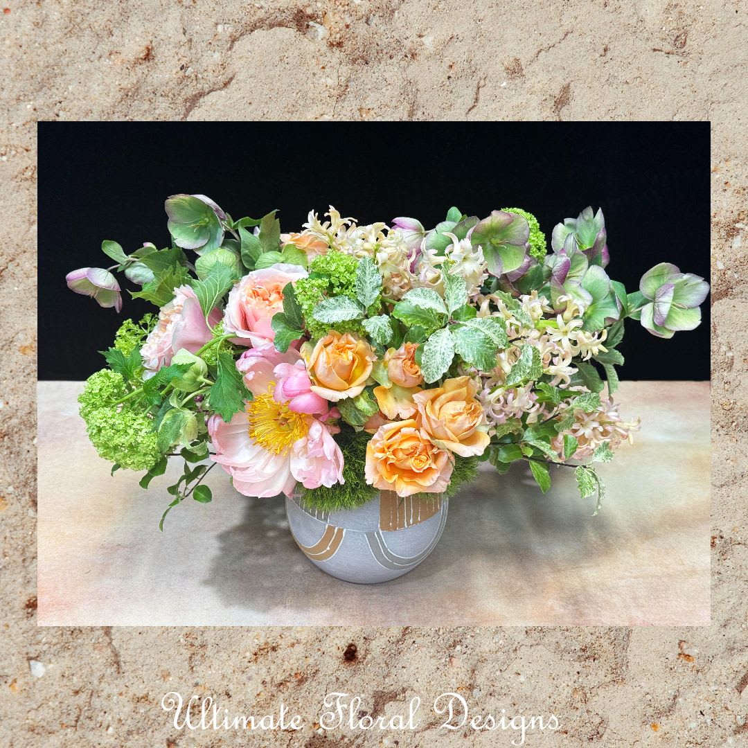 Whispers of Spring - Delicate, airy, and full of grace, Whispers of Spring captures the gentle beauty of the season. Creamy peach garden roses, pale pink peonies, lilac hyacinths, and hellebores flow effortlessly among textured greens and variegated foliage. Designed in a sleek art deco-inspired vase, this arrangement brings a refined charm to any setting—from elegant gatherings to quiet moments at home. A signature design by Ultimate Floral Designs.