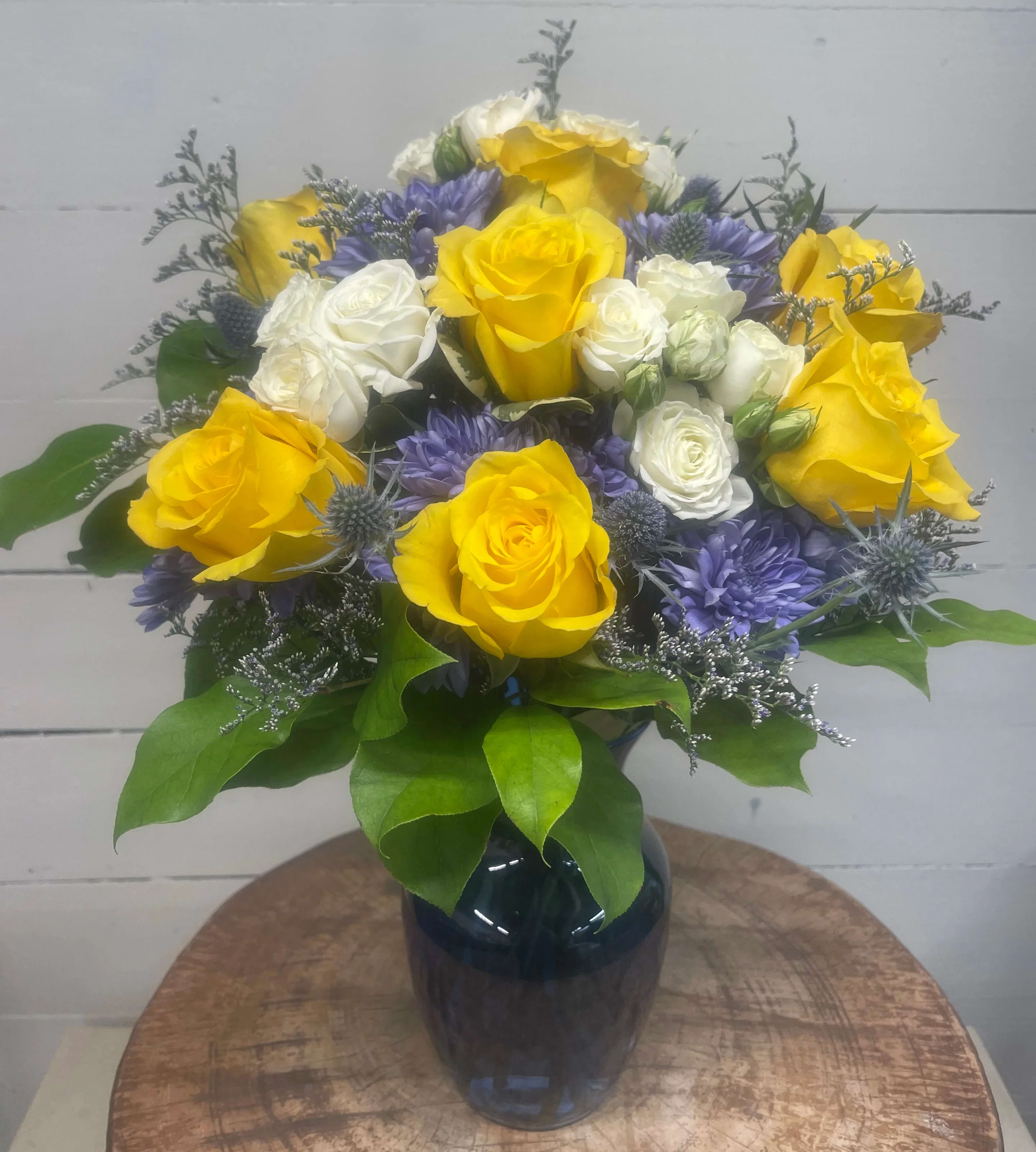 The Sun and The Moon  - Brighten the day with this arrangement which includes yellow roses, naturally blue chrysanthemums, and white spray roses. Arranged in an 8” tall blue vase.