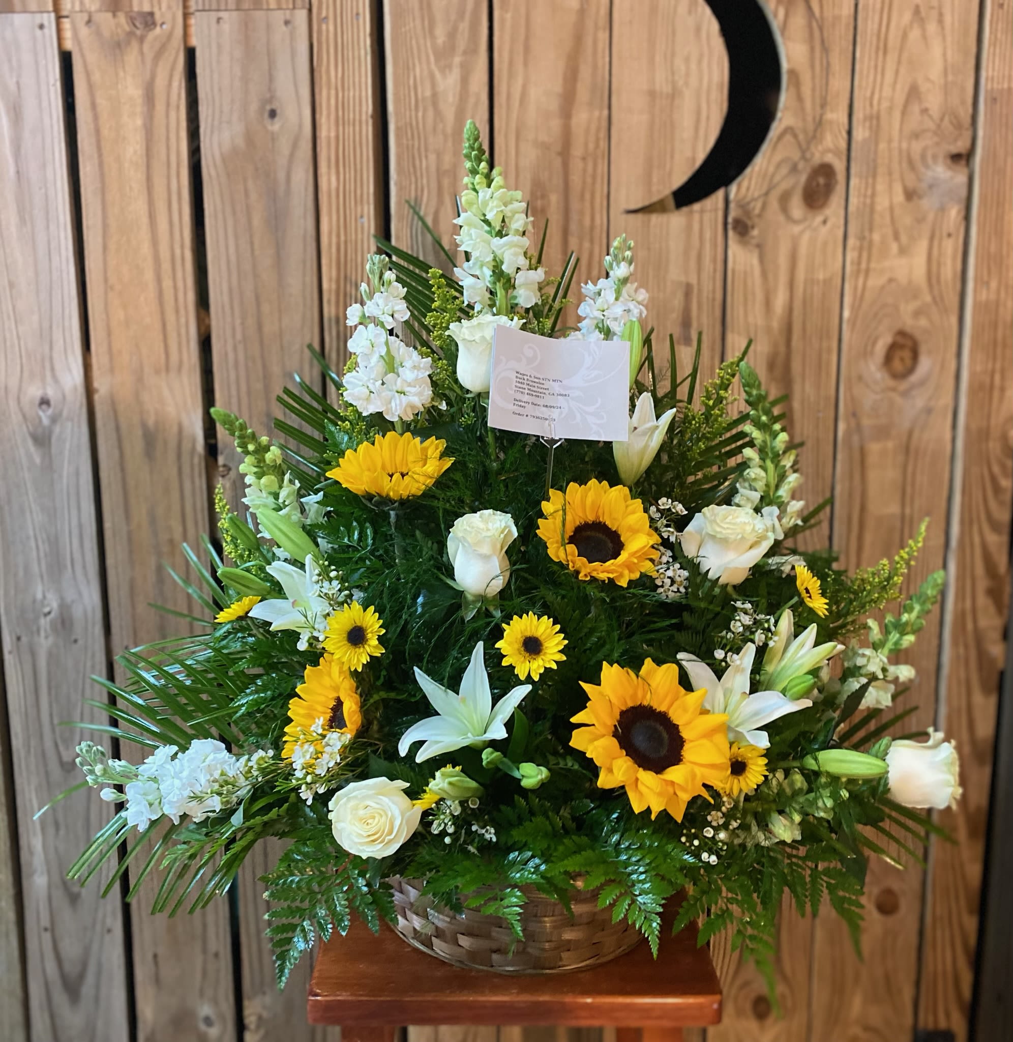 Hues Of Peace Basket / Urn Hues Of Peace Basket / Urn - White roses, sunflowers, lilies, snapdragons, stock, and yellow daisies accented with yellow saladago and wax flower arranged in your choice of an urn or basket.