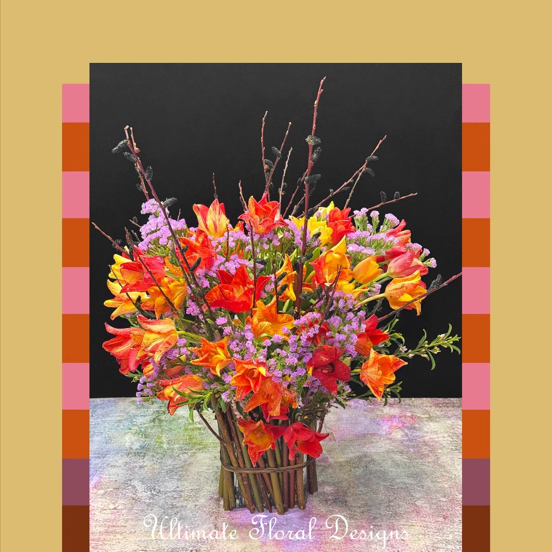 Wild Ember Glow - A striking display of fresh tulips in fiery shades of red, orange, and yellow, Wild Ember Glow is a vibrant arrangement full of energy and charm. Designed with natural branches and accented by seasonal filler flowers, this bouquet brings a lively, garden-inspired elegance to any space.  Please note: Tulip varieties and filler flowers may vary depending on seasonal availability at the time of ordering. Each arrangement will reflect the same bold and beautiful style.