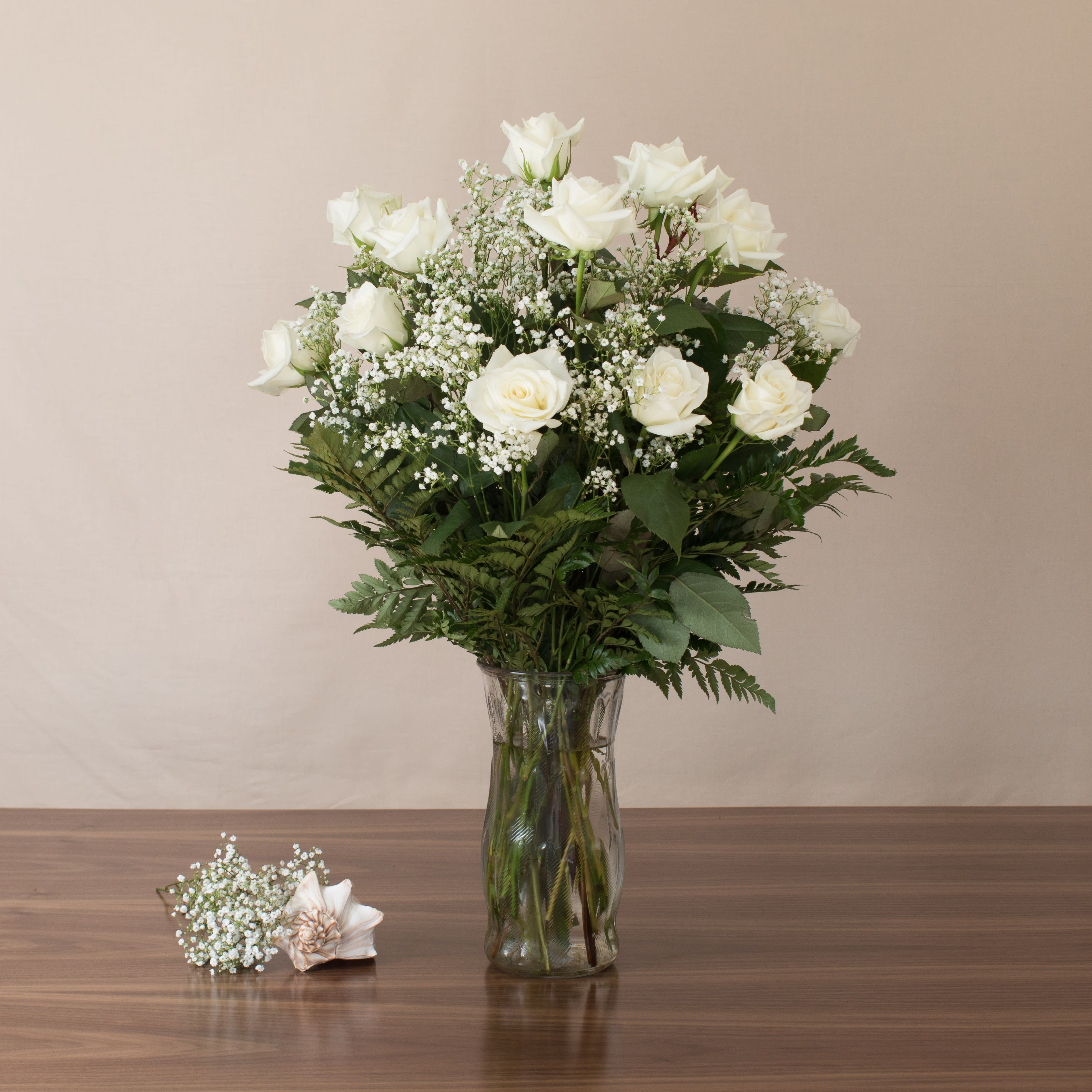 Watanabe White Rose Masterpiece - Serenity, calmness, purity – just a few words that come to mind when gazing upon these one dozen premium, long stem, white roses accented with lush greens and fillers. This arrangement captures the essence of tranquility and elegance, perfect for any occasion.    Key Features:    Premium White Roses: Features twelve exquisite long stem white roses, symbolizing purity and grace.    Lush Greens and Fillers: Enhanced with lush greens and fillers, adding texture and depth to the arrangement.    Emotional Elegance: Evokes feelings of serenity and calmness, making it an ideal choice for conveying heartfelt emotions.    Versatile Appeal: Suitable for various occasions, from celebrations to expressions of sympathy, offering timeless beauty.    Elegant Presentation: Expertly arranged to highlight the natural beauty and purity of white roses, ensuring a stunning visual impact.    Embrace serenity and purity with our Premium White Roses with Greens and Fillers, a timeless expression of elegance and grace.