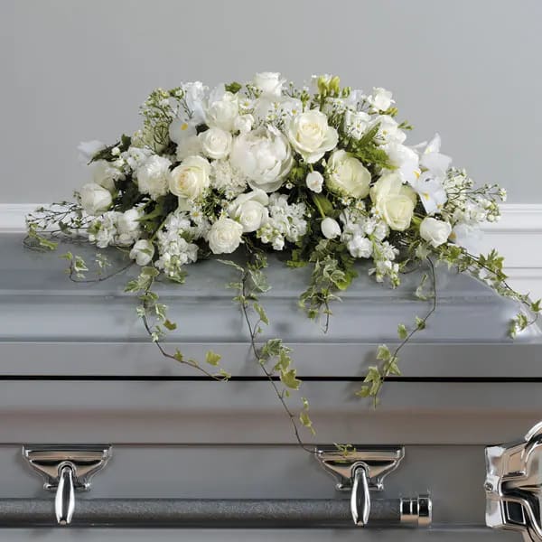 Loving Memories Casket Spray Loving Memories Casket Spray - This elegant all-white casket spray is a timeless expression of peace and purity, featuring graceful roses, iris, tulips, and carnations, accented with tenderly trailing greenery—offering a serene and heartfelt farewell.