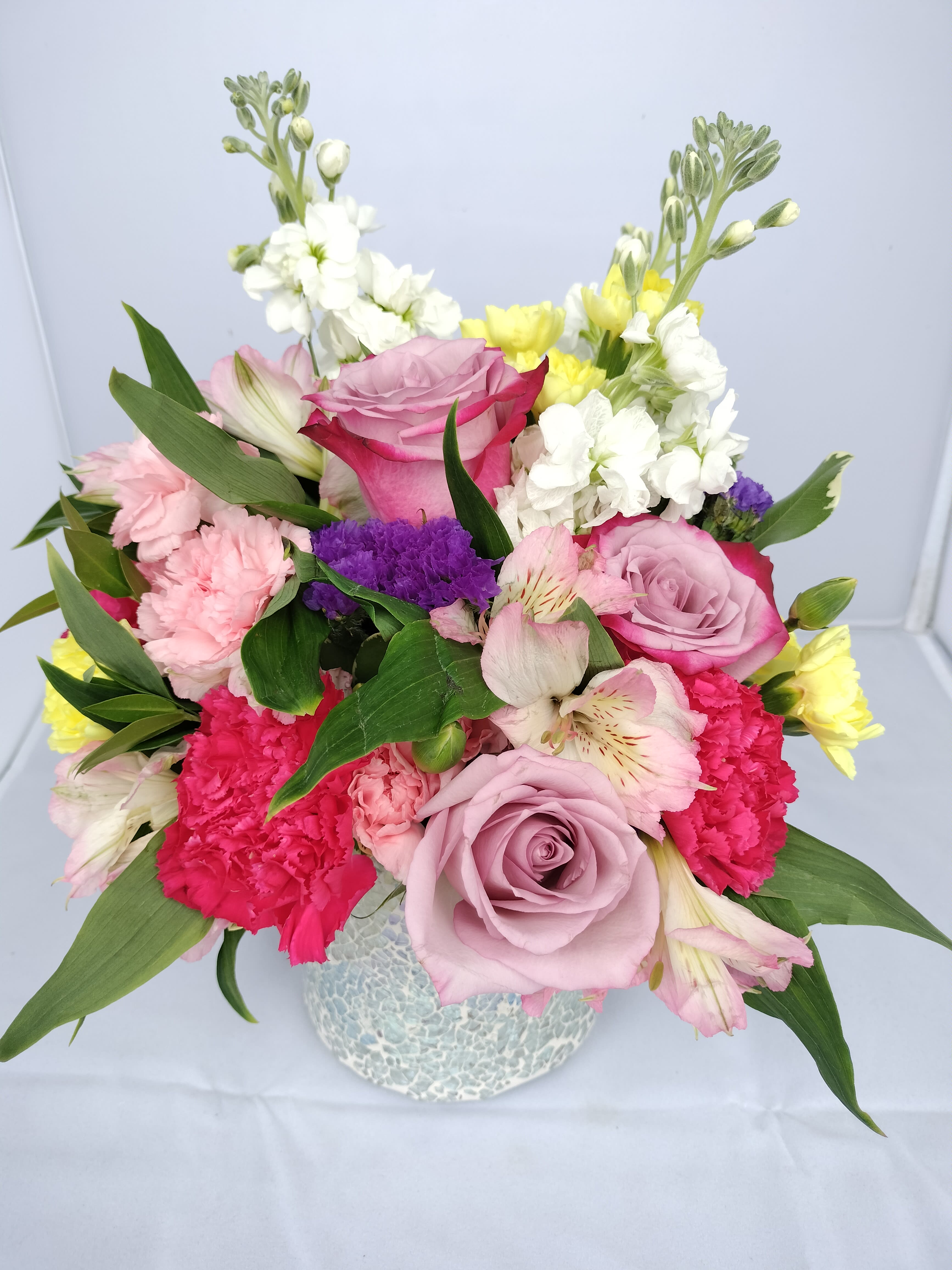 Fabulous Spring Colors in Iridescent Mosaic Glass Vase Fabulous Spring Colors in Iridescent Mosaic Glass Vase - This fabulous arrangement embodies spring with an array of colors of flowers in an iridescent mosaic glass cylinder vase. Features roses, carnations, stock, mini carnations, alstromeria and statice in combinations of pink, lavender and white.
