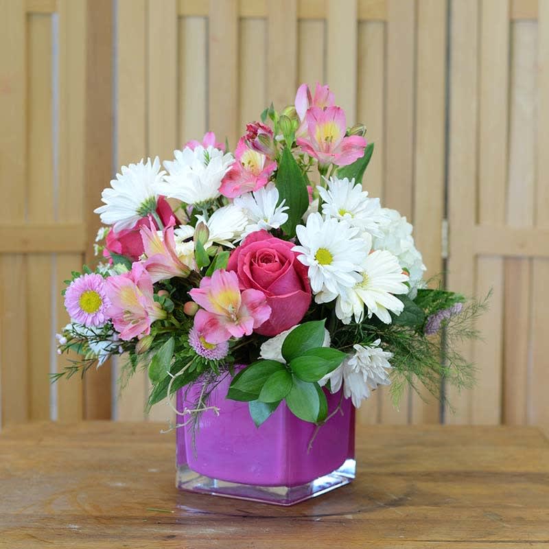 Pink Petal Cube Arr Pink Petal Cube Arr - This cute and dainty floral arrangement will warm your heart. Low cluster white daisies, hot pink roses and pink alstroemeria lilies. Cute and dainty.