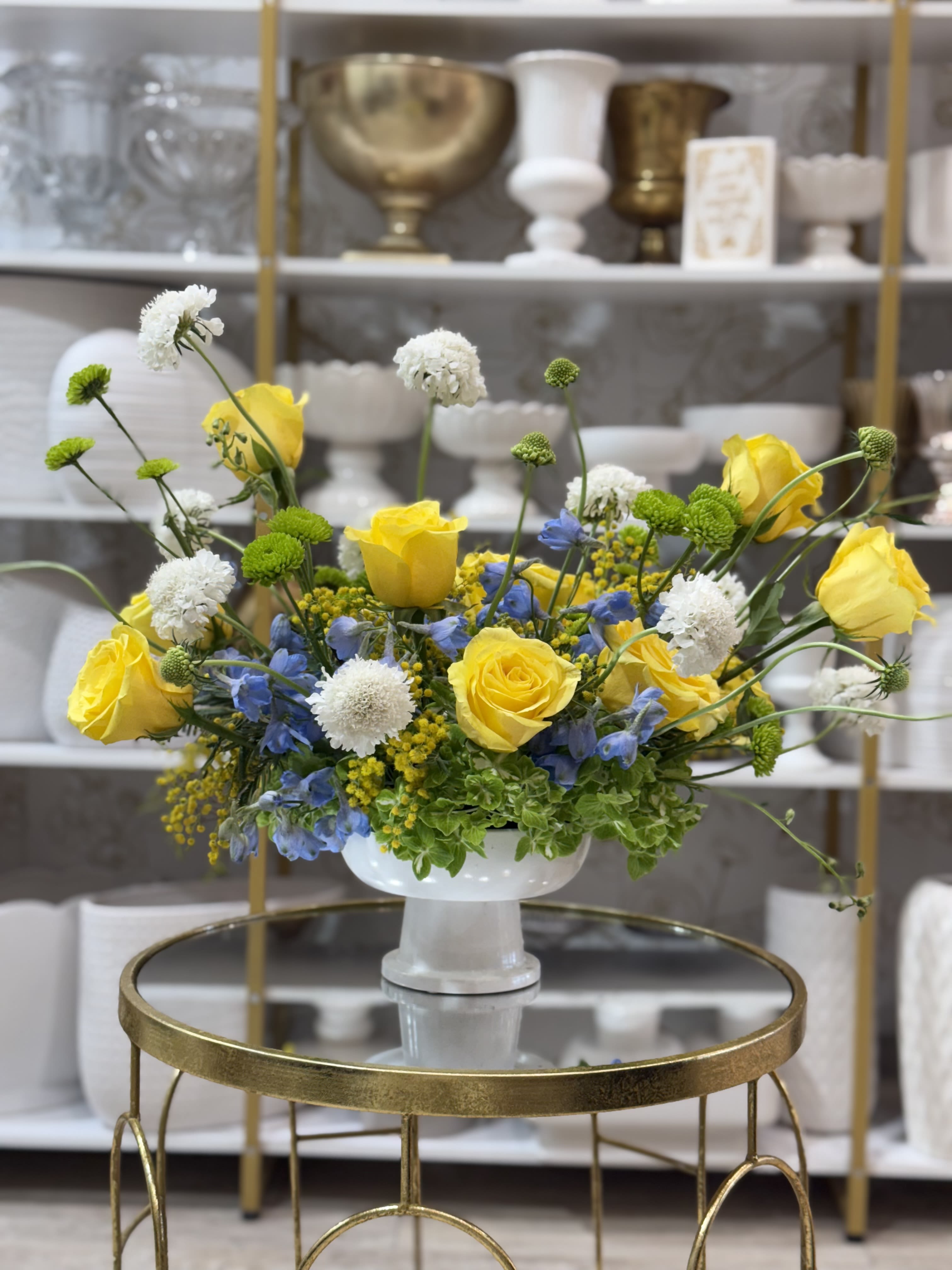 Floral Bliss Floral Bliss - Like a sunny sky captured in blue and yellow blooms (accented with a touch of puffy clouds)! Bright roses, blue delphinium, white hydrangeas, and more sitting pretty in a ceramic pedestal vase. A statement of joy and light sure to brighten anyone's day.