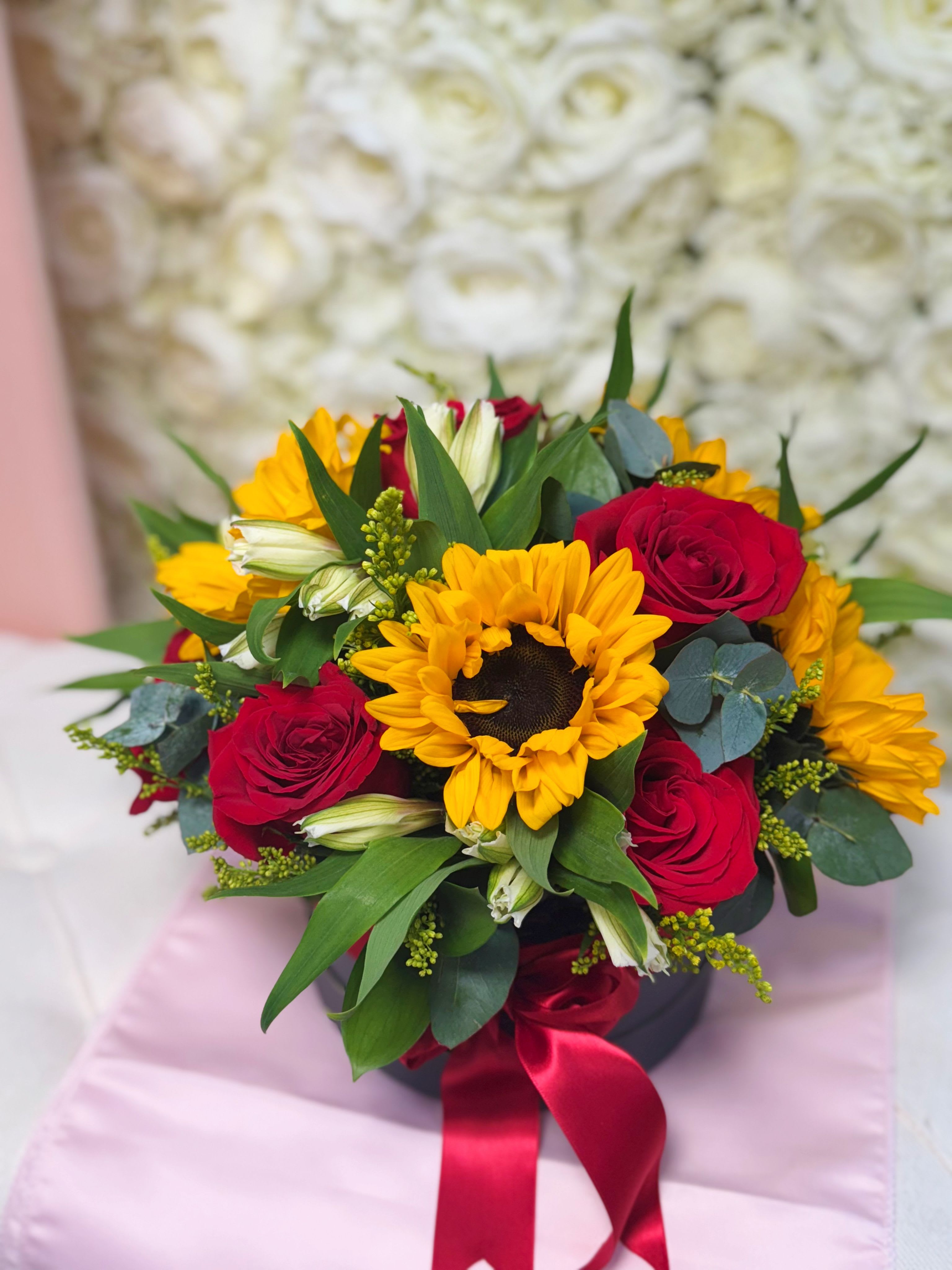 Shine of Love - A vibrant combination that expresses strength, joy, and passion. This elegant box with a red ribbon features a floral arrangement of sunflowers, red roses, white Astromelias, and fresh greenery. Perfect for delivering a message full of positive energy and unconditional love. 11”H x 12”W 