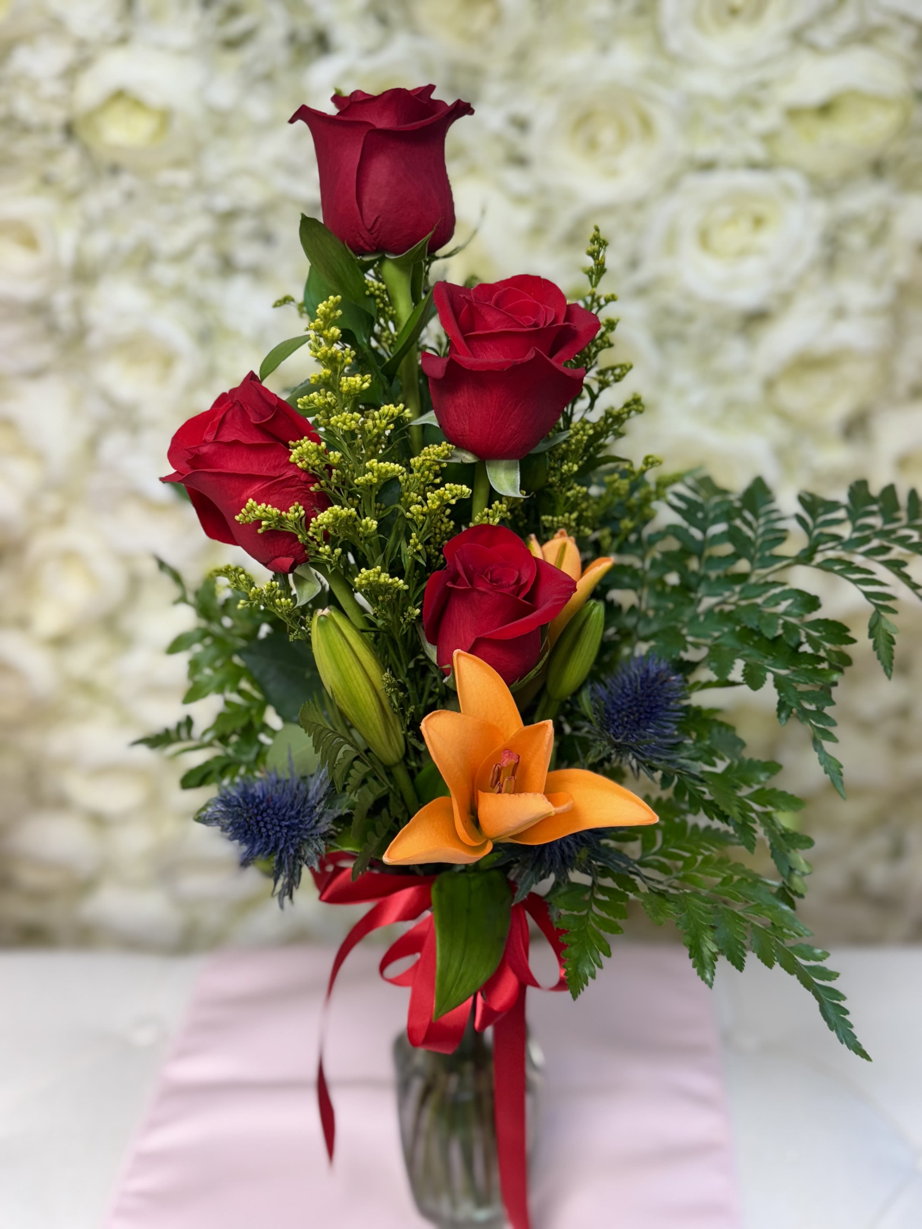 Touch of Fire Touch of Fire - A small arrangement full of life and color. This vase features four roses paired with vibrant orange lilies, creating a warm and energetic design. Perfect as a thoughtful gift, to show affection, or to brighten up any space with a touch of passion and joy.