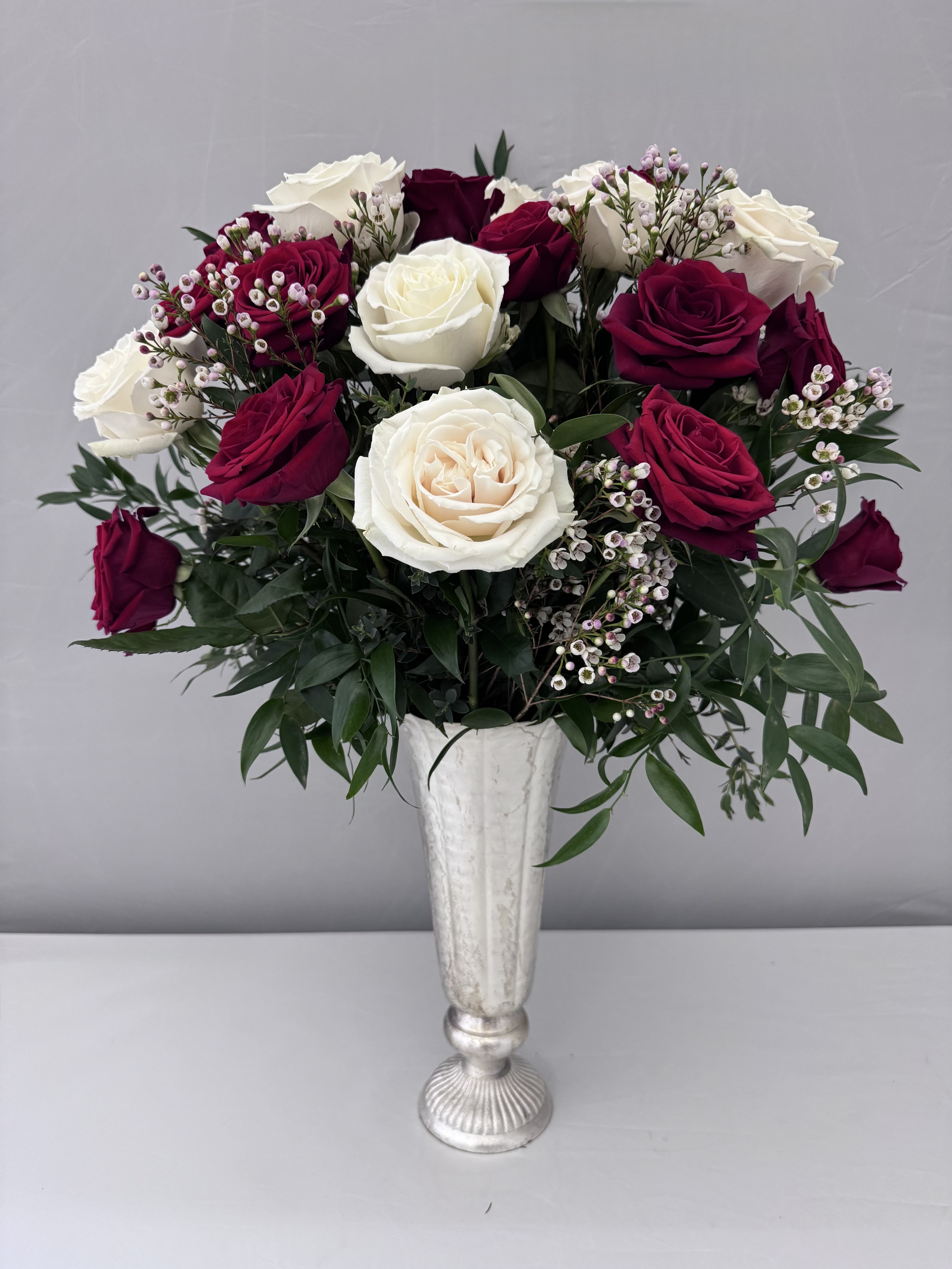 AMOUR  - A DOZEN RED AND WHITE ROSES SOPHISTICATELY ARRANGED WITH WHITE WAX FLOWER &amp; PREMIUM GREENERY, ITALIAN RUSCUS &amp; EUCALYPTUS IN A METAL LITA VASE FROM ACCENT DECOR.  VASE IS 6.5WX14.H. DELUXE:  18 ROSES RED &amp; WHITE MIXED  PREMIUM: 24 RED &amp; WHITE ROSES MIXED 