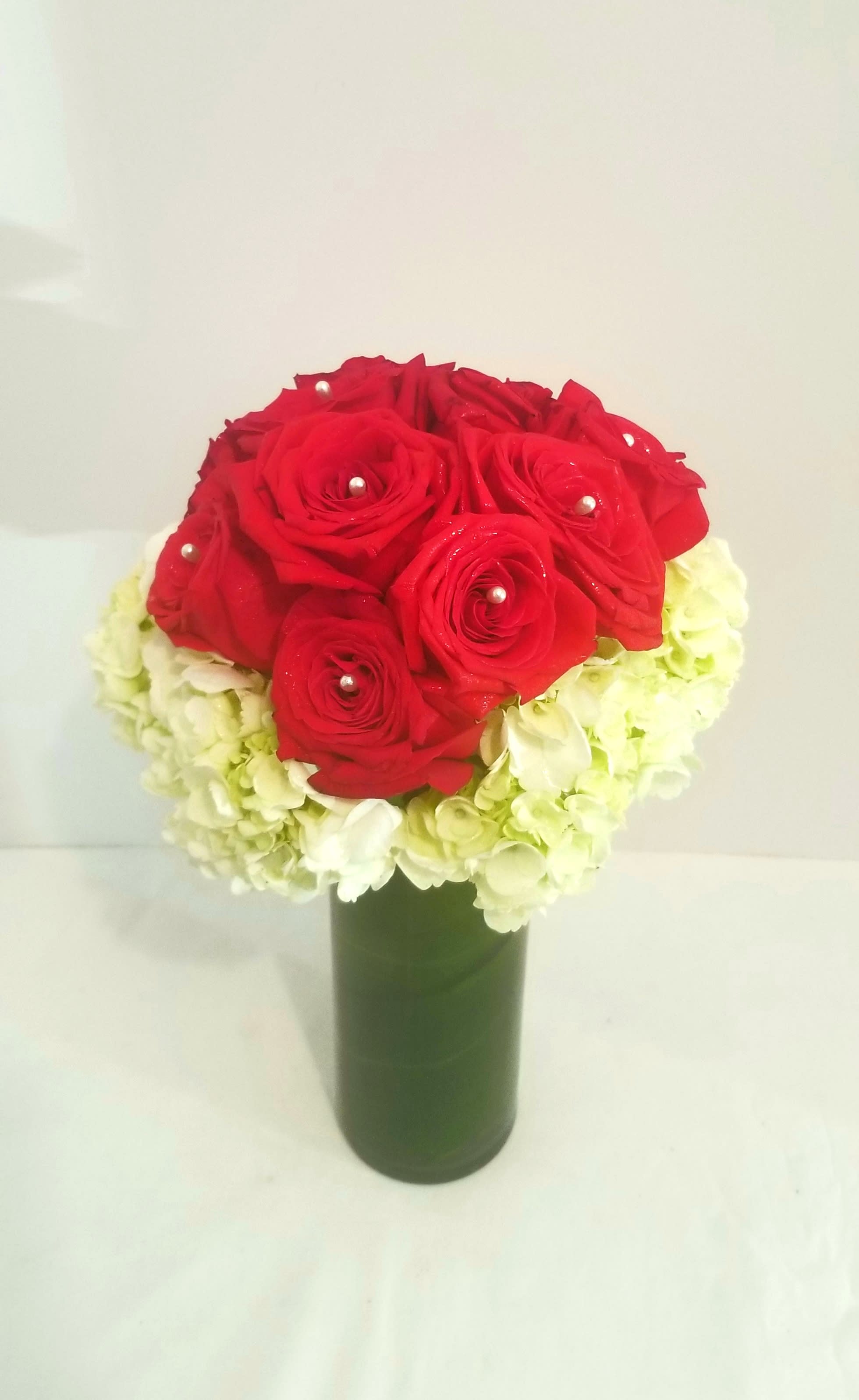 Alluring Roses - Send that special someone a beautiful bouquet of magnificent Red Rose's accented with Pearls, and Hydrangea in a slender cylinder vase with Aspidistra leaves. FlowerBee floral artist use only the freshest florals to create Alluring Roses. Regular contains a Dozen Rose's. Deluxe consisted of 18 Roses and Premium 24 Roses.  If you would like a color other than Red please specify in Special Instructions.