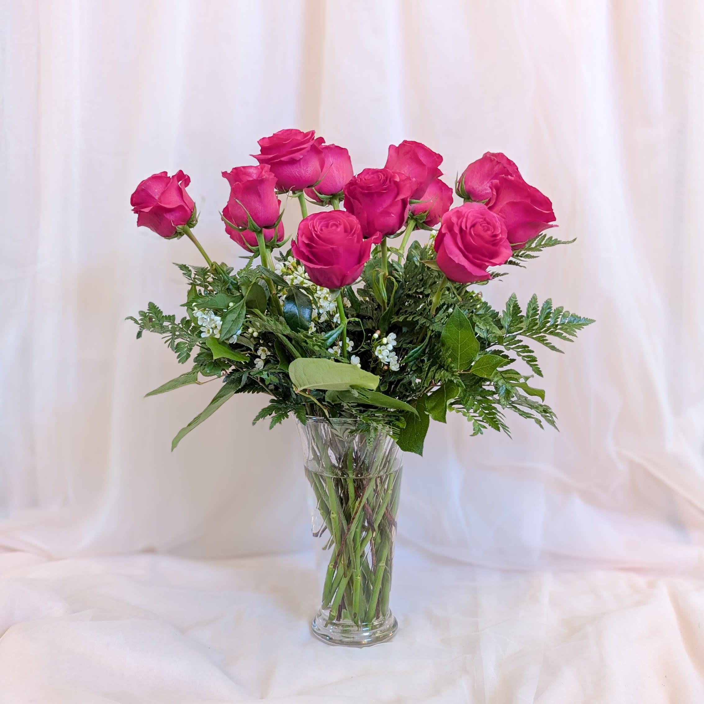 Hot Pink Rose Arrangement Hot Pink Rose Arrangement - This classic bouquet features a dozen vibrant hot pink roses elegantly arranged in a tall vase, complemented by lush greenery and delicate filler flowers. Perfect for any occasion, from anniversaries to birthdays or simply to brighten someone's day, this arrangement is a timeless expression of beauty and affection.