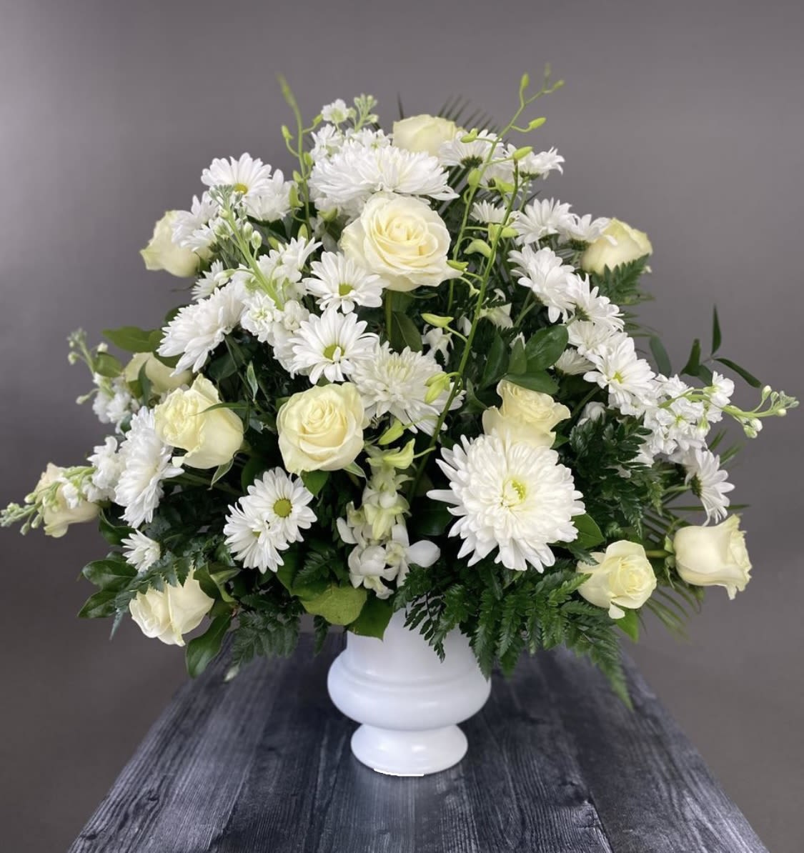 Round floral arrangements for funerals  - Round floral arrangement, on a white base, with roses, chrysanthemums, daisies, and fine foliages