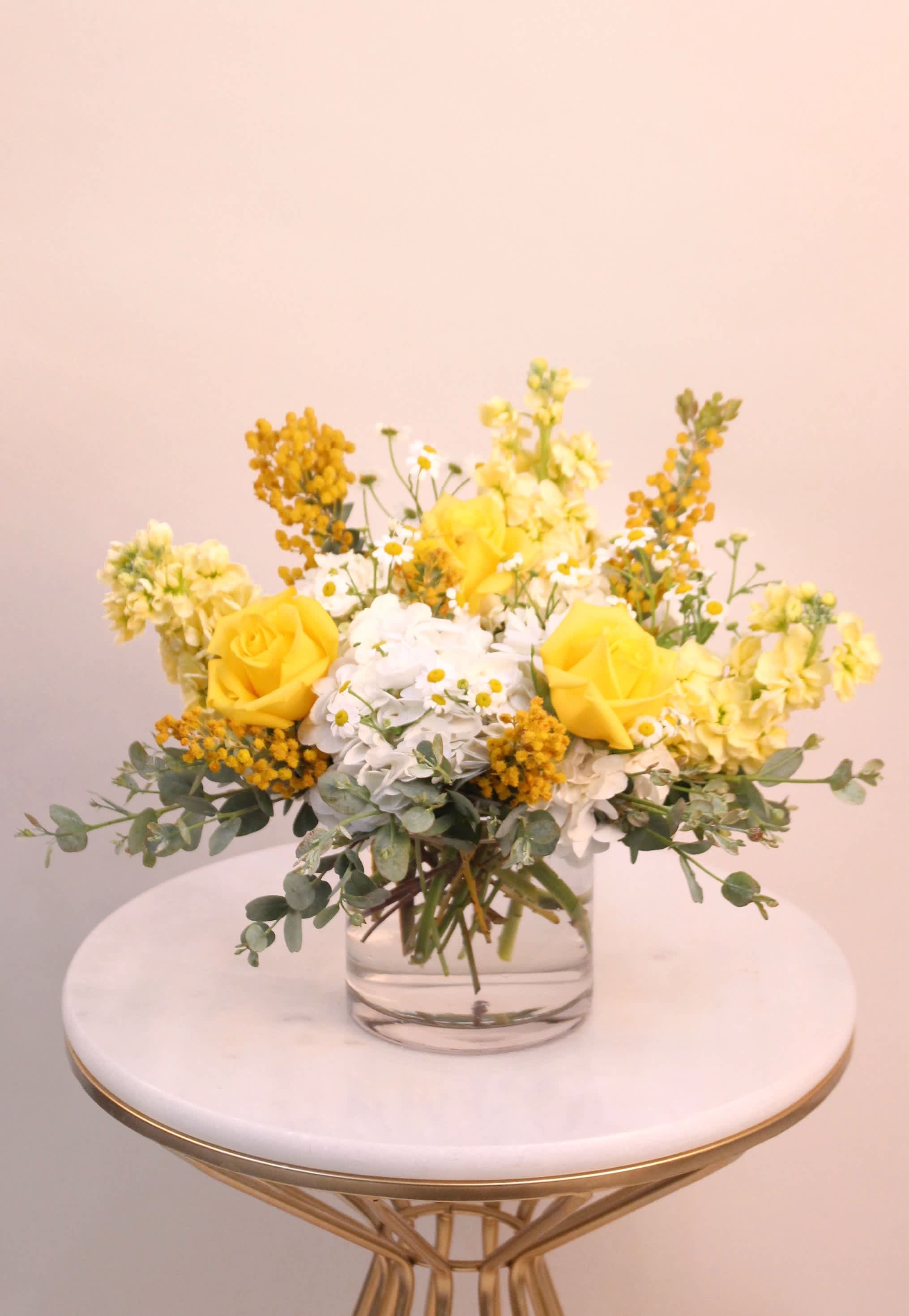 Lemon Spritz - A vibrant arrangement that boast with a beam of sunshine. This arrangement is designed in a clear glass cylinder vase, flowers may include hydrangeas, roses, stock, chamomile, mimosa and eucalyptus greenery.    Vase dimension: 5”W X 5”H