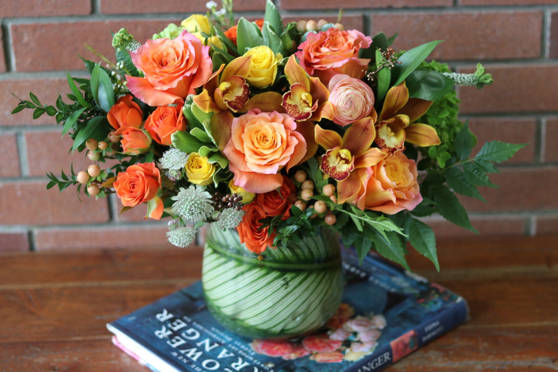 Modern Sunrise  - Introducing our stunning Modern Sunrise  bouquet, crafted by Venetian Flowers. This exquisite arrangement is a vibrant celebration of autumn, featuring a captivating mix of colors and textures. At its heart, you'll find striking orange cymbidium orchids, their unique shape adding elegance and sophistication. Surrounding them are free spirit garden roses and cheerful orange spray roses, which bring a lush, romantic feel to the bouquet.   The addition of delicate orange ranunculus adds a playful touch, while rose hip and rich fall foliage provide depth and a nod to the seasonal transition. Completing this beautiful ensemble are the soft white tweedia blooms, which create a lovely contrast and enhance the overall brightness of the arrangement.   Presented in a modern vase, this bouquet is not only a feast for the eyes but also a perfect gift for any occasion or a stunning centerpiece for your home. Experience the warmth and beauty of &quot;Autumn Radiance&quot; and bring a touch of autumn elegance into your space.