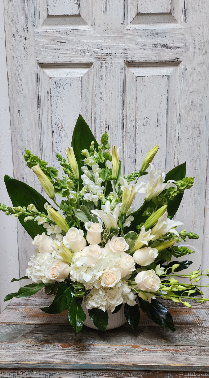 Hope by BloomNation™ Hope by BloomNation™ - An all-white arrangement with roses, delphinium orchids, and more framed by a backdrop of large leaves. Suitable for any type of funeral ceremony