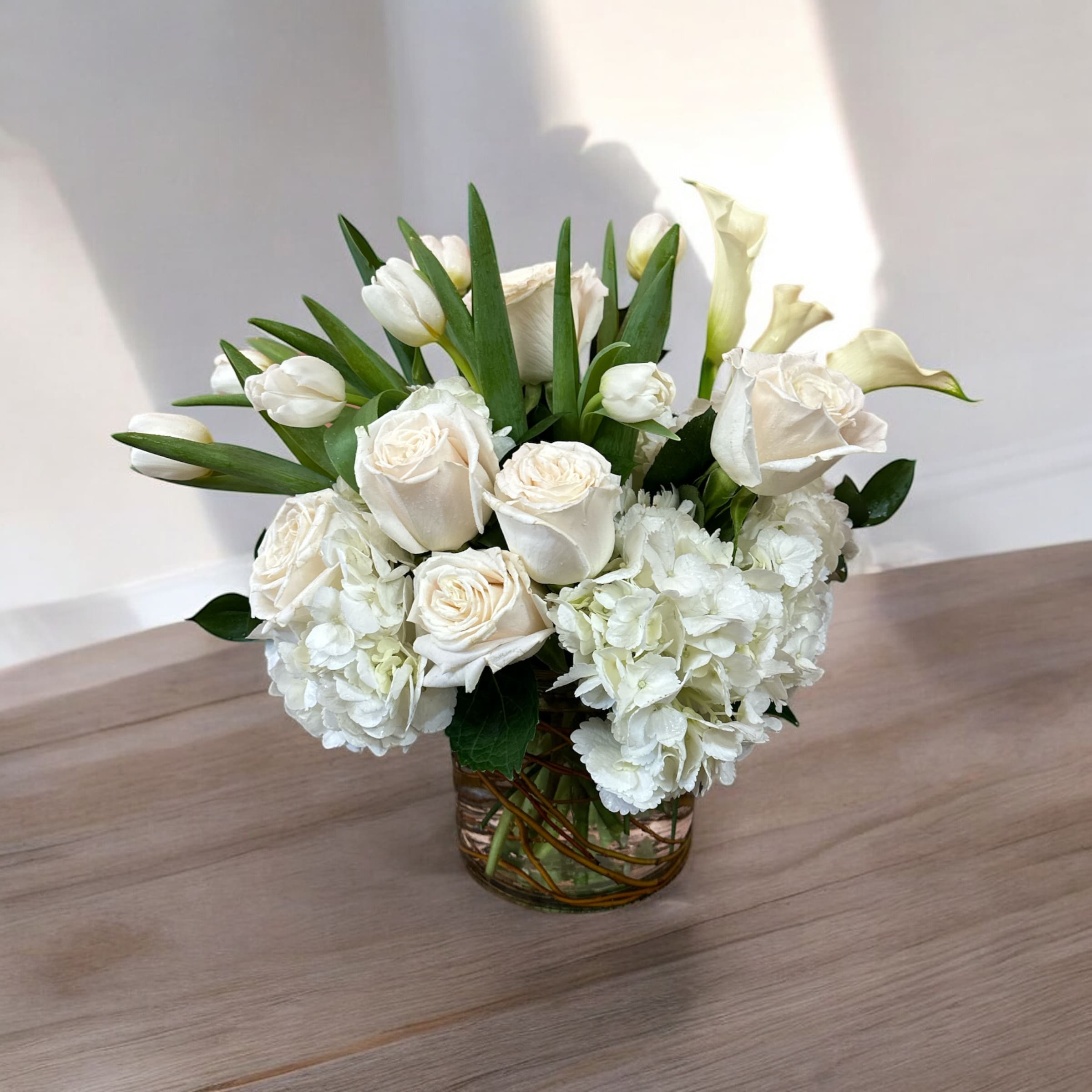 Classic Whites  - This elegant all-white design is a perfect fit for any occasion. Featuring white roses, miniature calla lilies, white tulips and hydrangeas in a round cylinder vase with curly willow tips, this magnificent bouquet will stand out with an added touch of sophistication and luxury to any home or office. 
