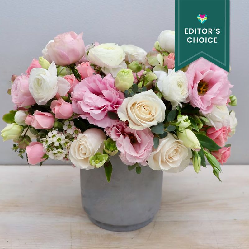 Miss Pinky - LA - Editor's Choice - This stunning arrangement features white ranunculus, soft pink lisianthus, and an assortment of roses accompanied with seasonal greenery. The standard size stands at about 10-12 inches.