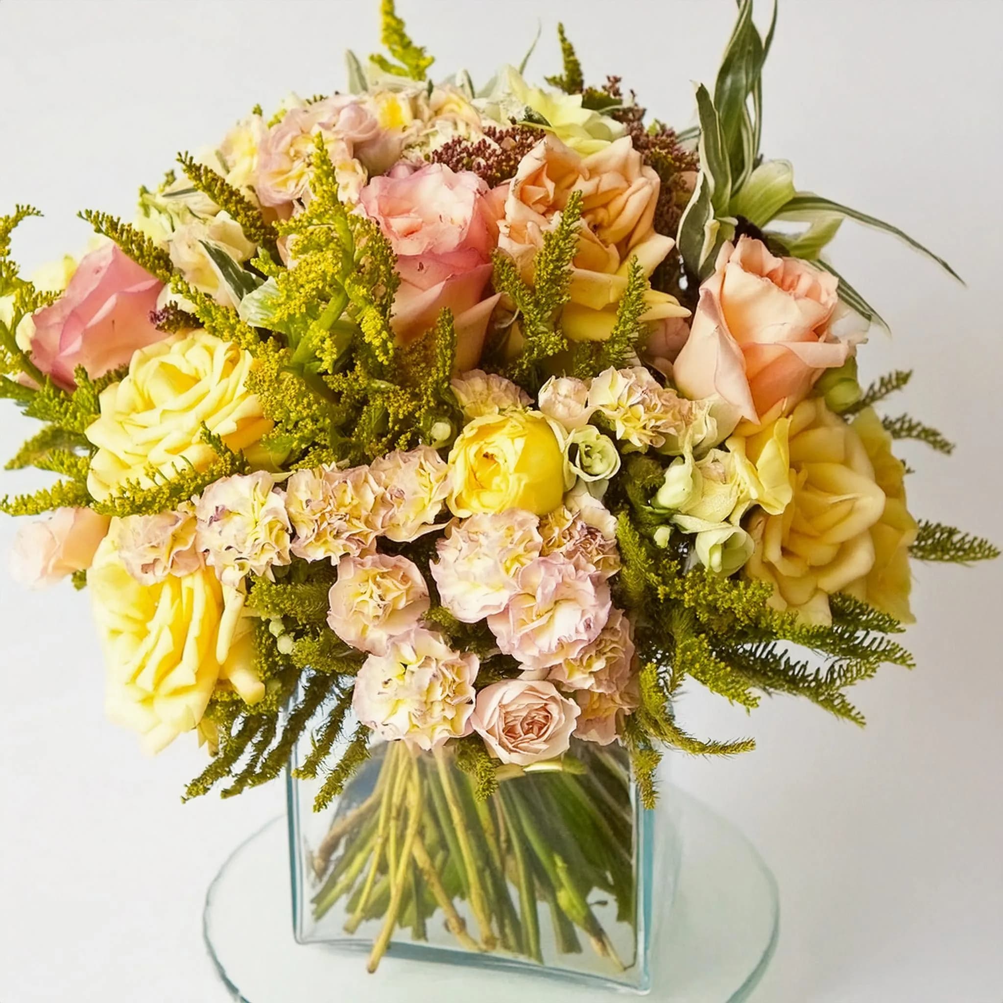 Sunlit Serenity Bouquet - The Sunlit Serenity Bouquet is a breathtaking arrangement designed to bring a touch of elegance and warmth to any space. Featuring a harmonious blend of pastel roses, delicate carnations, and lush greenery, this bouquet exudes a sense of tranquility and beauty. Housed in a modern glass cube vase, the Sunlit Serenity Bouquet is perfect for any occasion, whether it’s celebrating a special moment or simply brightening up your day. Each arrangement is thoughtfully crafted to ensure the highest quality and freshness, making it a stunning centerpiece for your home or a heartfelt gift for a loved one.