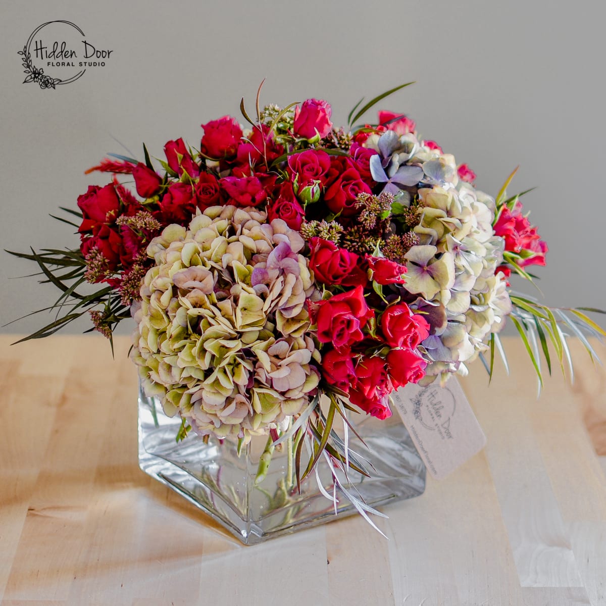 Pretty in Pink Pretty in Pink - The vivid hot pink spray roses steal the spotlight, radiating energy and exuberance. Each bloom is a testament to beauty and resilience, captivating the eye with its rich color and charming petals. These roses symbolize passion and admiration, making them ideal for expressing heartfelt emotions on any occasion. Complementing the spray roses are the delicate antique hydrangeas, their soft hues contrasting the vibrant pinks. The hydrangeas exude elegance with their full, luscious blooms and intricate details. The combination of hot pink spray roses and antique hydrangeas creates a harmonious balance, evoking a sense of beauty and sophistication. The arrangement is lovingly arranged in a square vase, adding a touch of modernity and refinement. Whether placed as a captivating centerpiece or gifted as a romantic gesture, "Pretty in Pink" commands attention and exudes charm in any setting.