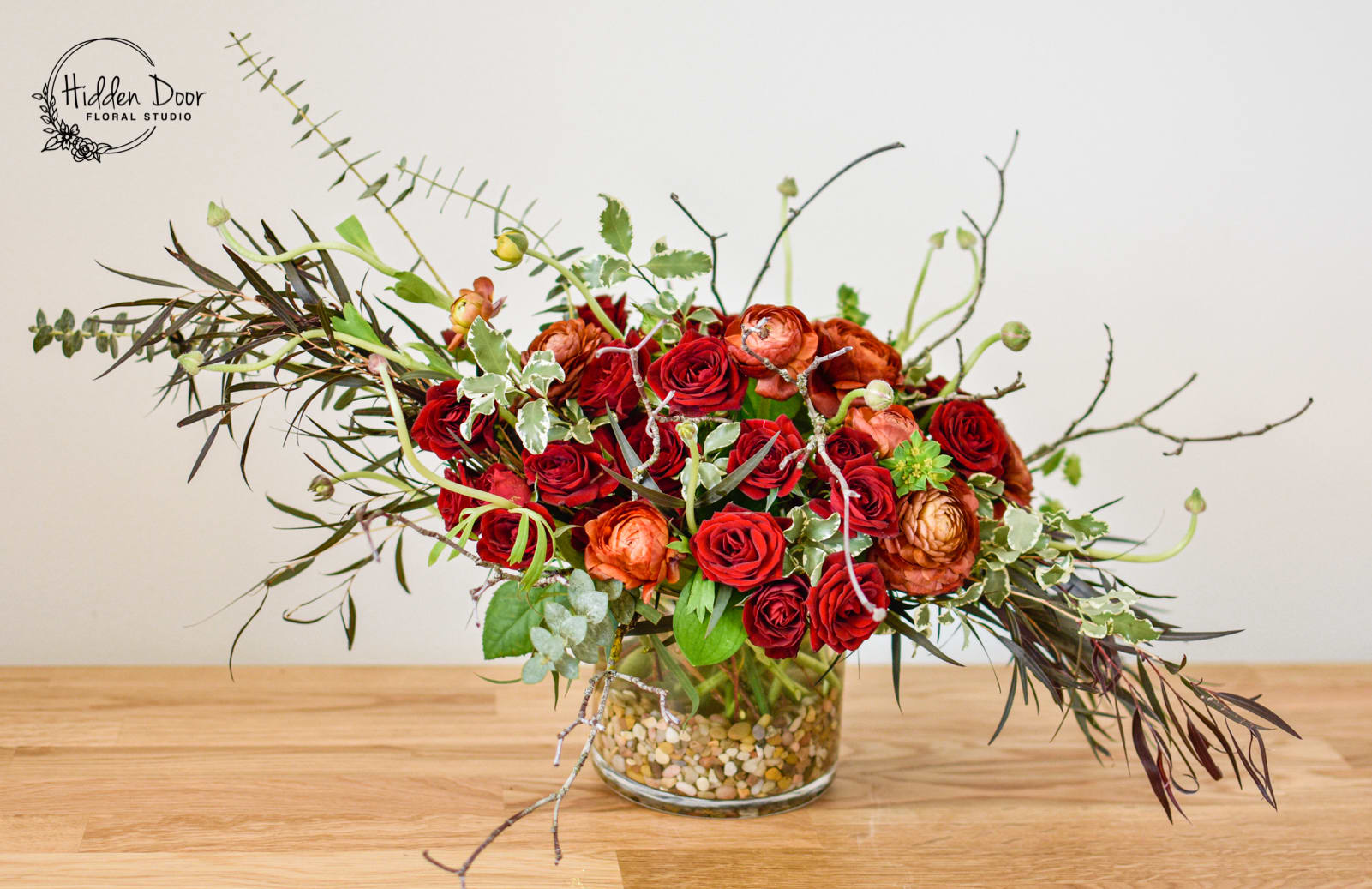 The English Garden The English Garden - This floral arrangement breaks away from conventional symmetry and embraces the natural beauty and asymmetrical charm that defines a wild and flourishing garden. Inspired by the untamed allure of nature, "The English Garden" exudes an air of organic floral elegance. Nestled in a clear glass vase, this beautiful floral arrangement captures the essence of a blooming garden. Dark red spray roses and red or orange ranunculus take center stage, infusing the floral collection with vibrant hues and a touch of romance. The interplay of these exquisite blooms with delicate twigs and seasonal greens creates a harmonious fusion of floral textures and vibrant colors, mirroring the untamed beauty of a wild, hidden garden. "The English Garden" is a true work of art, with each flower arrangement being a masterpiece in its own right. Like the ever-changing nature of a wild floral garden, every floral creation is guaranteed to be a unique floral design, adding to the overall allure and capturing the essence of nature and art. This individuality makes it a truly exceptional floral gift, celebrating the beauty found in the natural world.