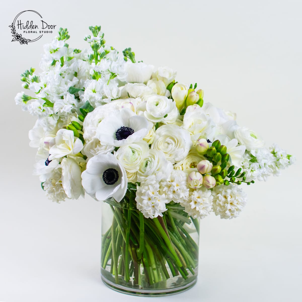 Elegant White -  This captivating bouquet is a true masterpiece that exudes class, sophistication, and pure luxury. Prepare to be dazzled as you immerse yourself in a symphony of pristine white roses, delicate ranunculus, fragrant hyacinths, enchanting stocks, gorgeous anemones, and delightful freesias.  As you indulge in the exquisite beauty of &quot;Elegant White,&quot; a delightful fragrance envelops the air, enchanting your senses and creating a truly immersive experience. The sweet scent of freesias, the alluring aroma of hyacinth, and the delicate perfumes of stocks and roses intertwine, enhancing the elegance of this magnificent arrangement.  This unique floral design is not your everyday ordinary floral bouquet. &quot;Elegant White&quot; is a grand display of nature's most splendid blooms, meticulously handcrafted to create a statement piece that commands attention. Each bloom is carefully selected for its pristine beauty, representing the epitome of grace and refinement.  At Hidden Door Floral Studio, we take pride in our commitment to excellence, ensuring that every &quot;Elegant White&quot; arrangement is meticulously crafted to perfection. Our skilled florists pour their expertise and passion into each and every detail, creating a floral arrangement that is truly exquisite and unrivaled in its beauty.  