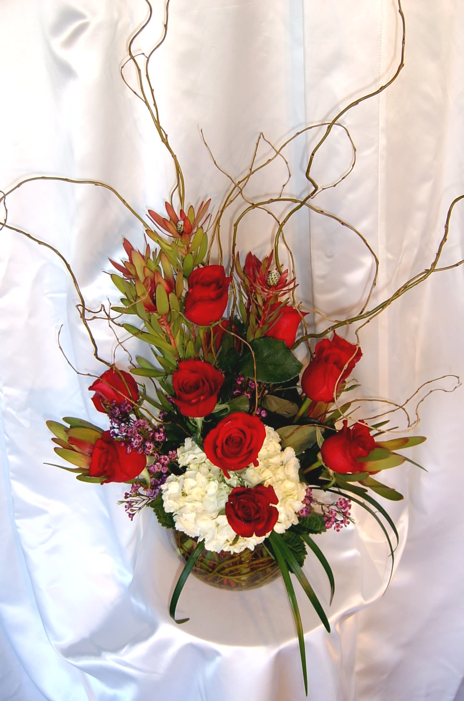 Roses Hydrangea Bowl Roses Hydrangea Bowl - Our biggest and most plump premium red roses are featured in this exquisite modern rose design. If you are looking for high end design, this is the arrangement to order - long lasting romantic flowers artfully arranged in a web of willow and a clear glass bowl. 10 premium large red roses- or your choice of color if you order at least a week prior! Also included: large creamy hydrangea blossom, exotic safari sunset jester protea, wax flower, curly willow and lily grass.* Substitutions will be made if necessary. Exceptional gift for the holidays, Mother's day or Valentine's day.