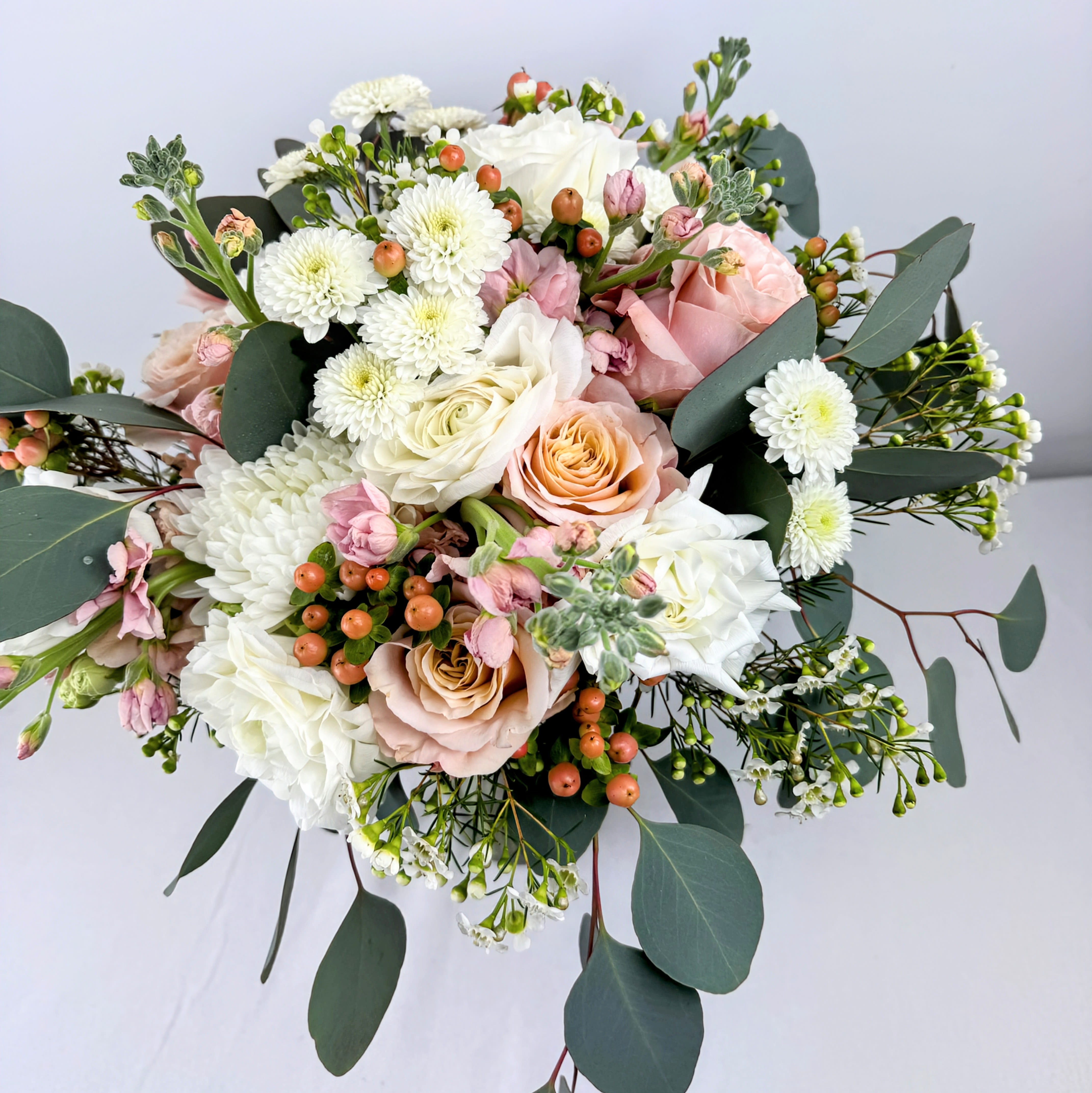 Bridal Bouquet Blushing Beauty - This beautiful hand tied bouquet was created using roses, ranunculus, stock, hypericum berries, mums, wax flower and lush greens. Let us help you design your dream bouquet!