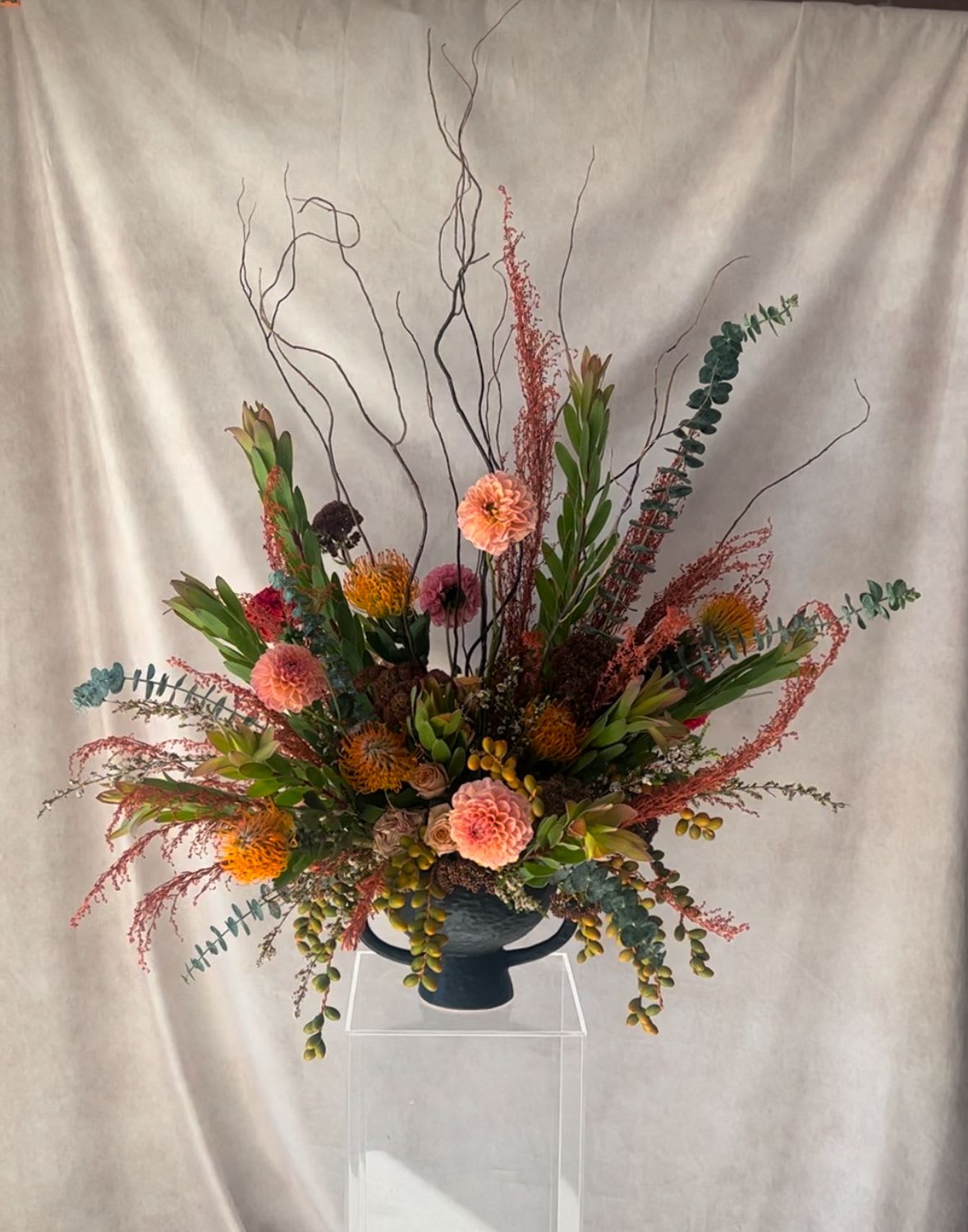 Harvest Moon  - &quot;Harvest Moon&quot; Floral Arrangement Moody and magnetic, Harvest Moon is an ode to twilight skies and the quiet romance of autumn nights. A rich medley of warm tones and textural depth is artfully arranged in a sleek black vase, creating a striking silhouette. This design captures the glow of a golden moonrise—elegant, mysterious, and deeply emotive. Perfect for adding a touch of seasonal magic and soulful beauty to any space.