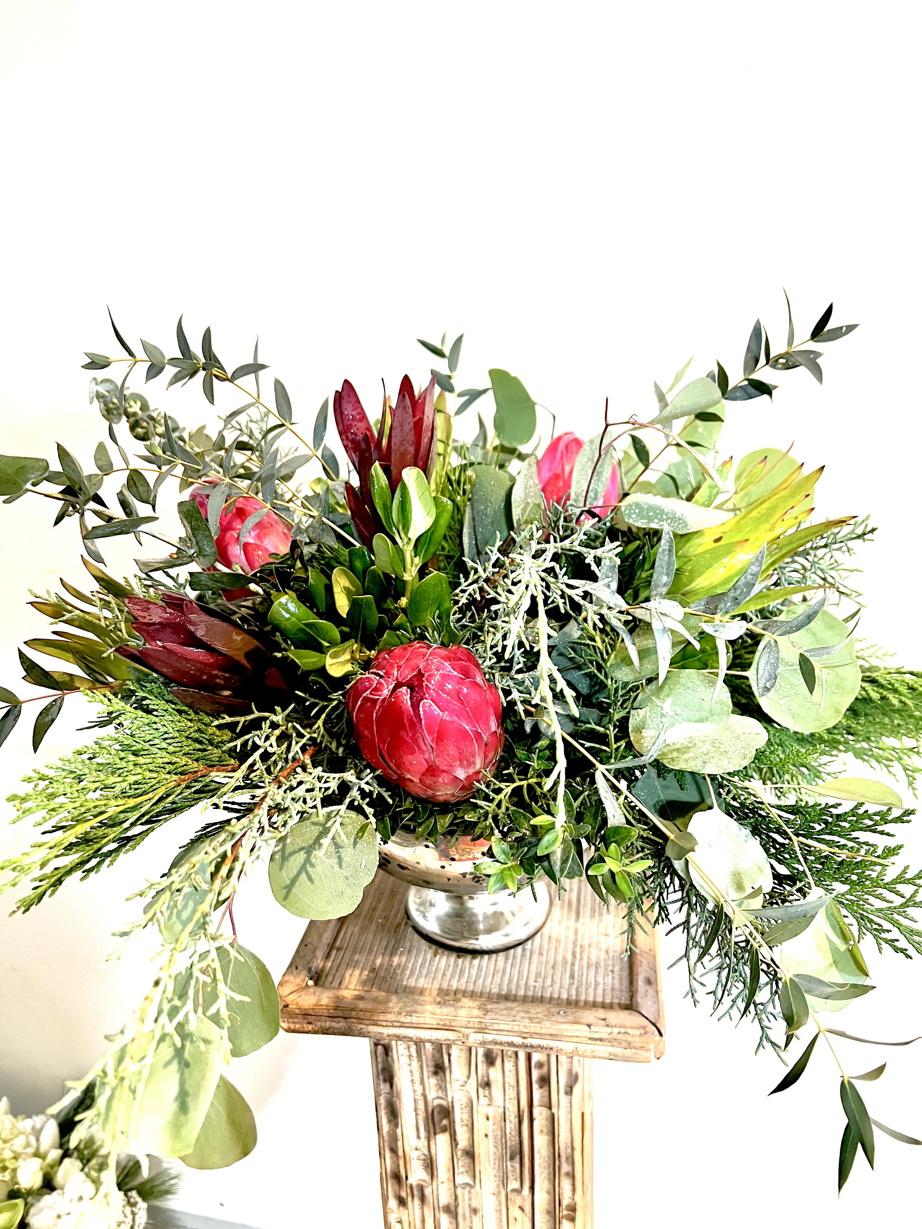 Natural and elegant Natural and elegant - A beautiful centerpiece, arranged in a mercury, glass dish filled with natural greenery and mink Proteas. Sure to bring enjoyment long after the holidays have passed.