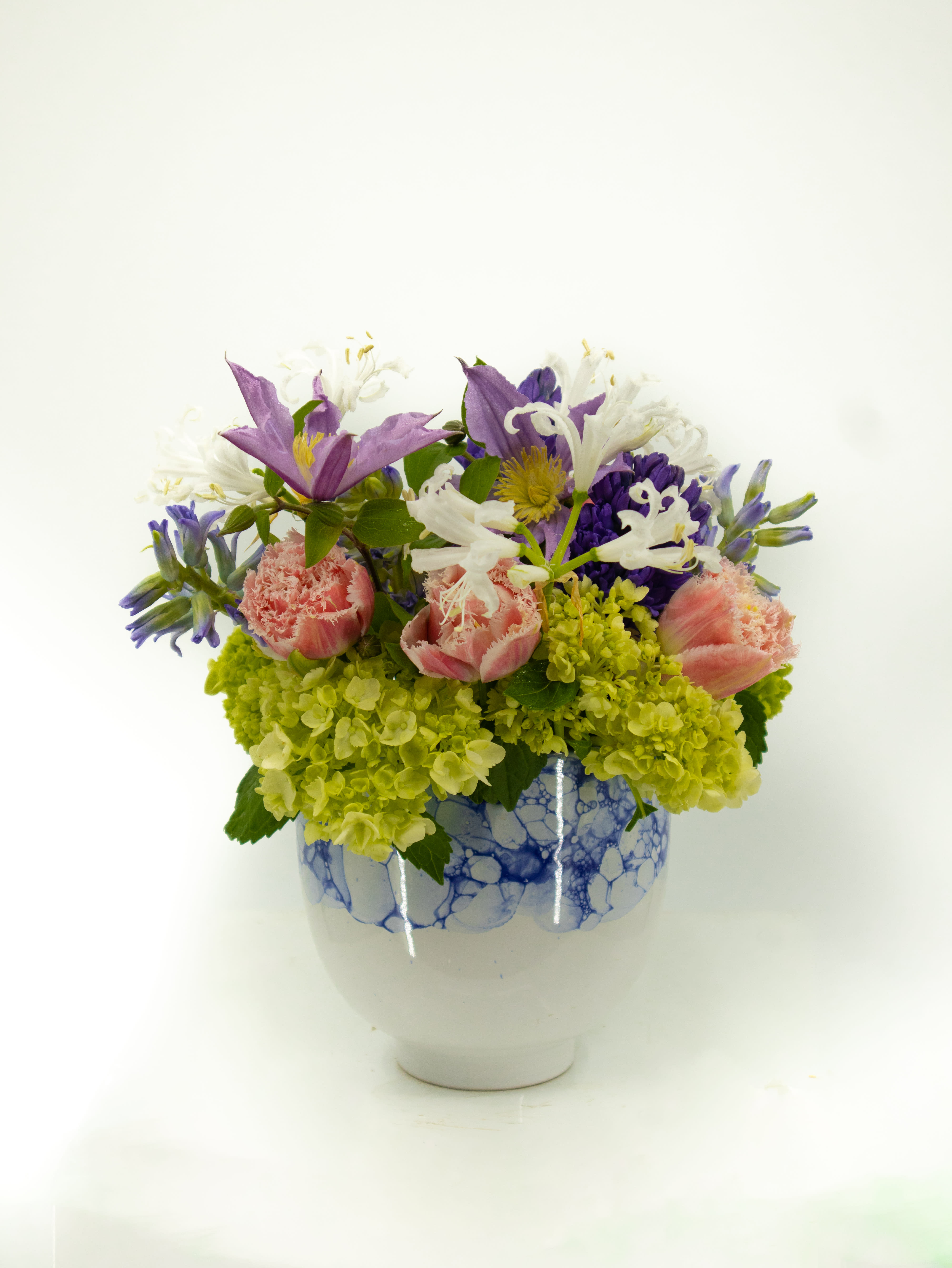 Dora Dora - This short yet impactful arrangement will catch anybody's eye. Filled with hydrangeas tulips, and other seasonal flowers. This arrangement will be sure to give any space a lovely energy. The the stunning vase lends itself well to the dramatic look and fullness of the arrangement.