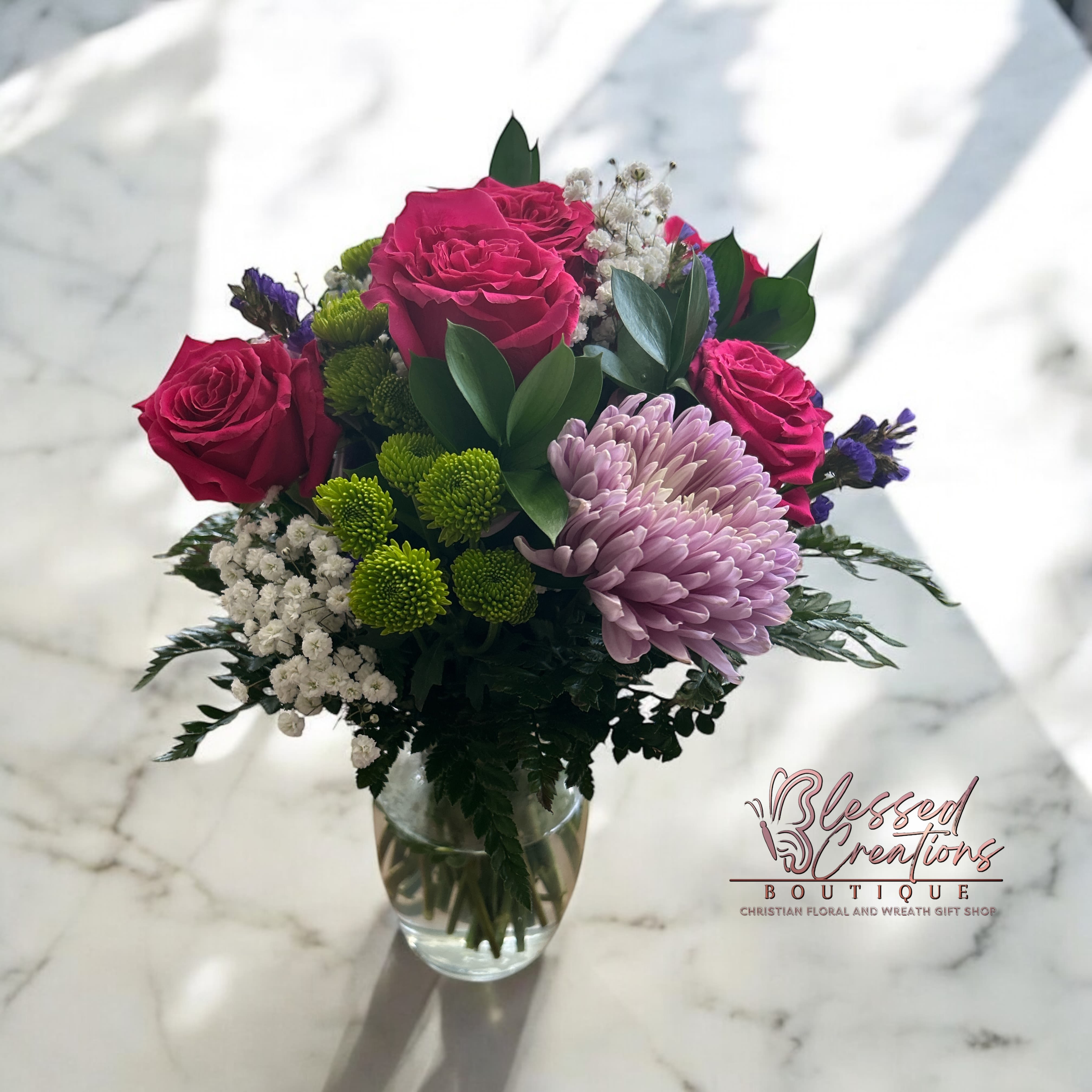 Floral testament Floral testament - Brighten any space with this bold and beautiful design. Featuring hot pink roses cheerful green Pom Pom buttons, purple chrysanthemums and lush greenery. A beautiful blend of color and charm arranged in a stylish vase. It’s a perfect way to celebrate, uplift, or add a touch of life to someone.