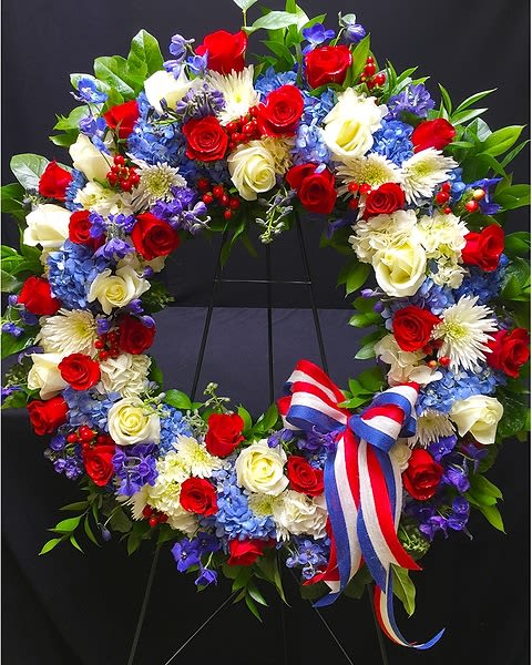 American Tribute - This Patriotic Wreath is paved with seasonal flowers, hydrangea and roses in Red, White and Blue. It is finished off with red, white &amp; blue ribbon and presented on a 5' tall easel. For substitution of flowers or color, please call the store at 858-454-0146.  All prices in USD ($)