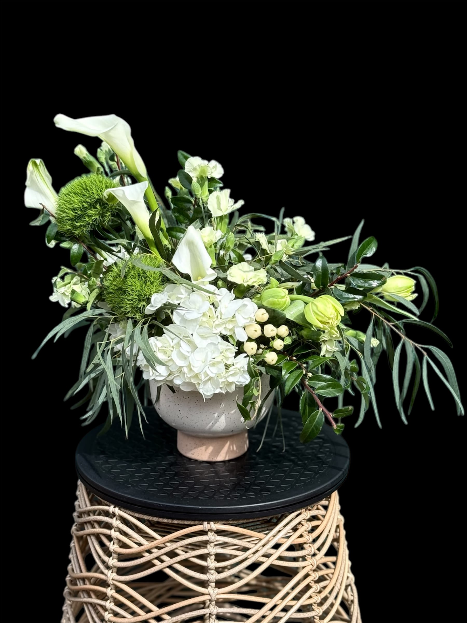 Emerald Garden - This elegant and modern arrangement emphasizes on balance of form, color, and texture creating a harmonious and eye-catching display and is sure to catch anyone's breath. This gorgeous piece is versatile and suited for various occasions, from everyday decor to special events like weddings or sympathy arrangements. These beauties are placed in a neutral-toned vase that complements the flowers without overshadowing them, featuring white flowers including hydrangeas, calla lilies, along with green accents from foliage and other green flowers. 